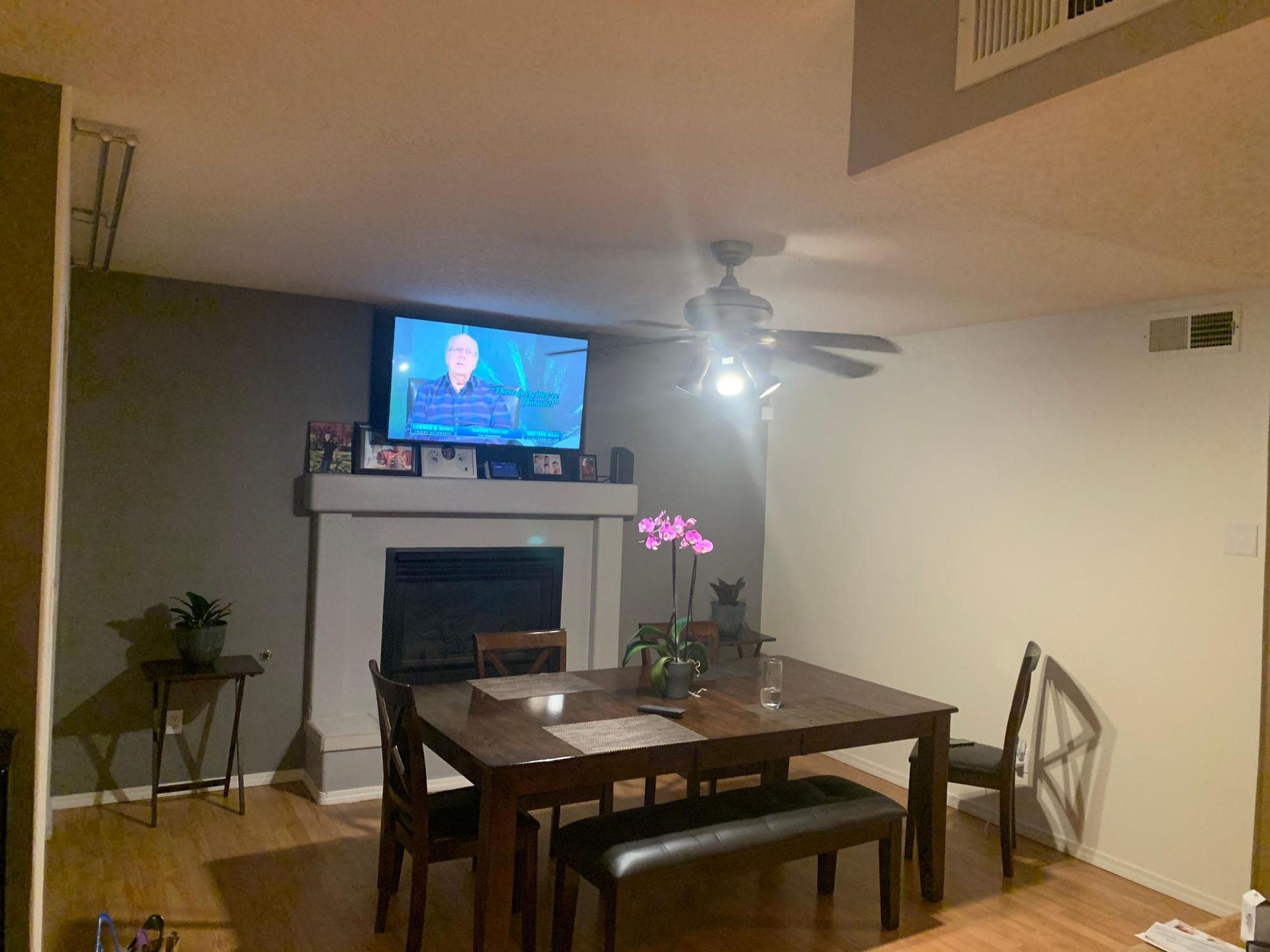 Dining room with table and bench facing a TV above a fireplace in a modern living space