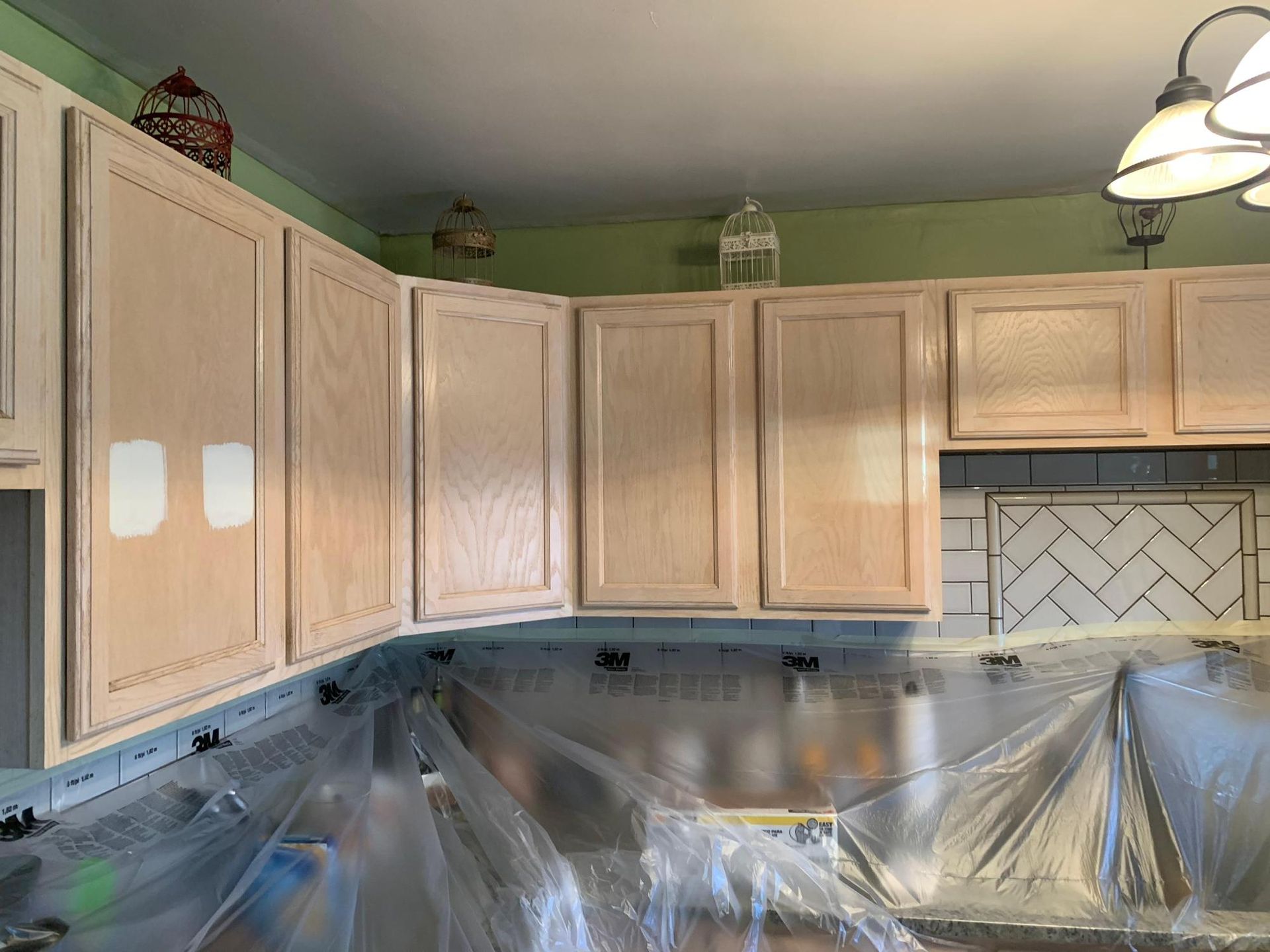 Kitchen with light wood cabinets, green walls, and counters covered in protective plastic during renovation