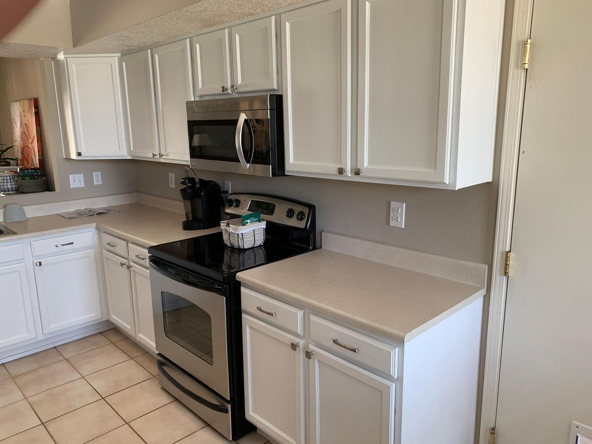 Modern kitchen with white cabinets, stainless steel appliances, and beige tile flooring