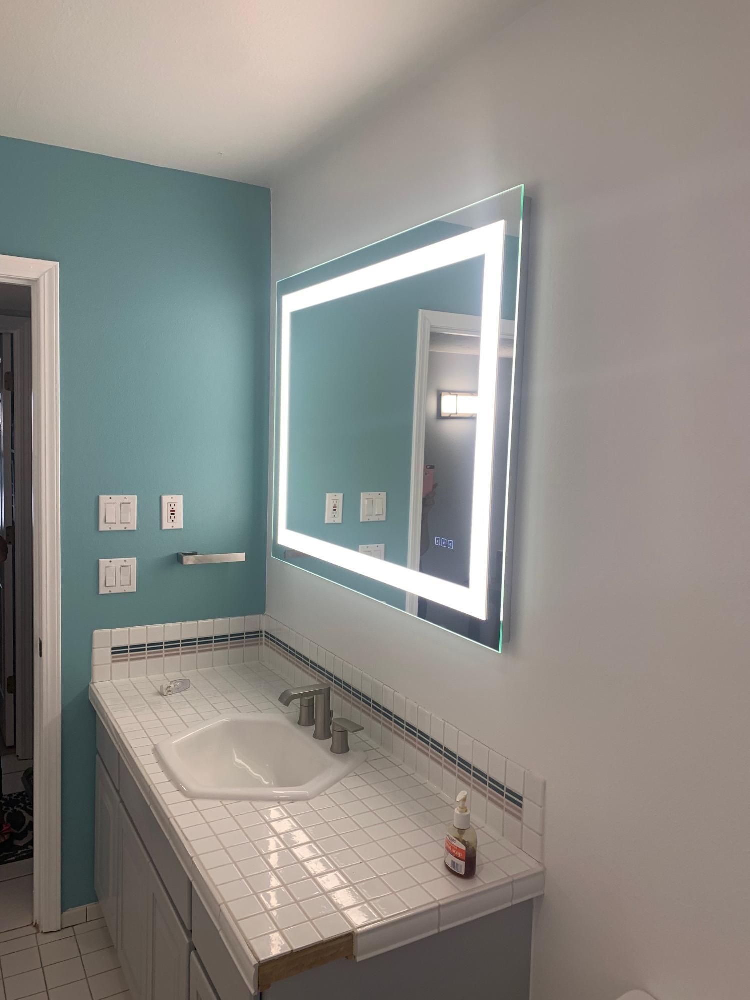 Bathroom vanity with lit mirror, white countertop, and teal walls.