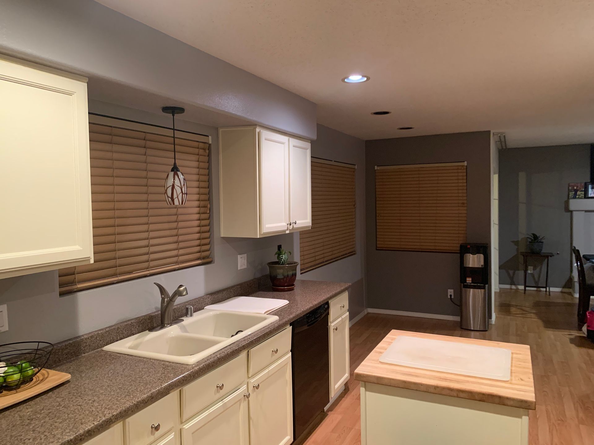 Modern kitchen with white cabinets, granite counters, sink, island, and blinds over the windows
