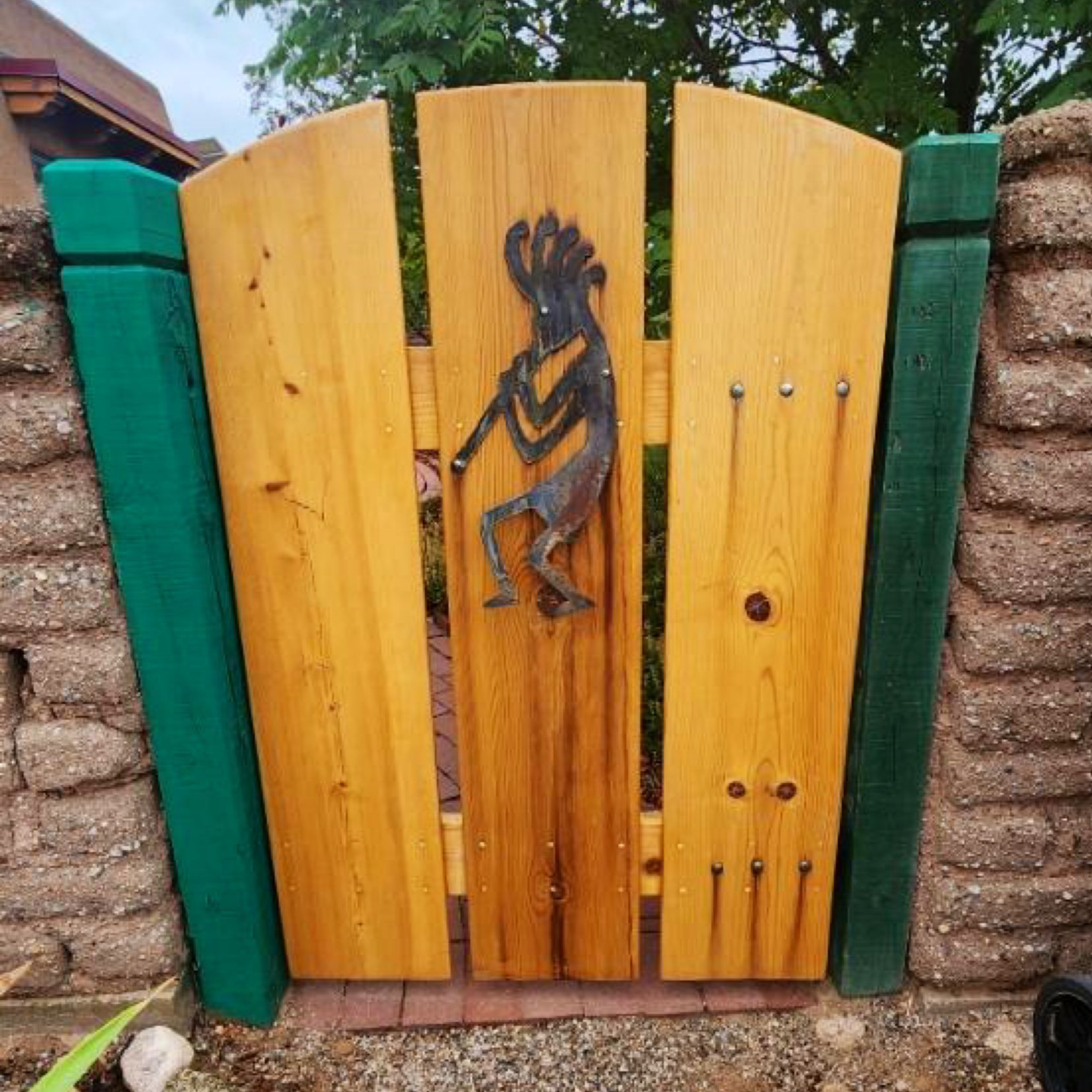 Colorful wooden gate with carved bird decoration between green fence posts and brick walls