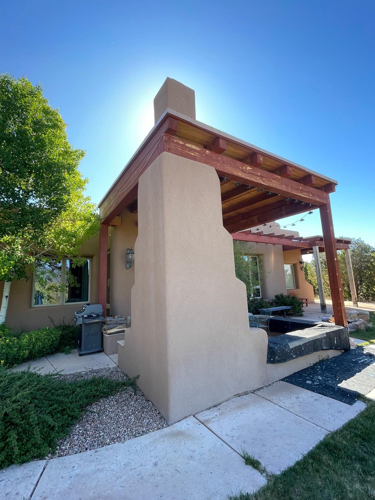 Stucco house entrance with a wooden pergola, beige columns, and a sunny walkway