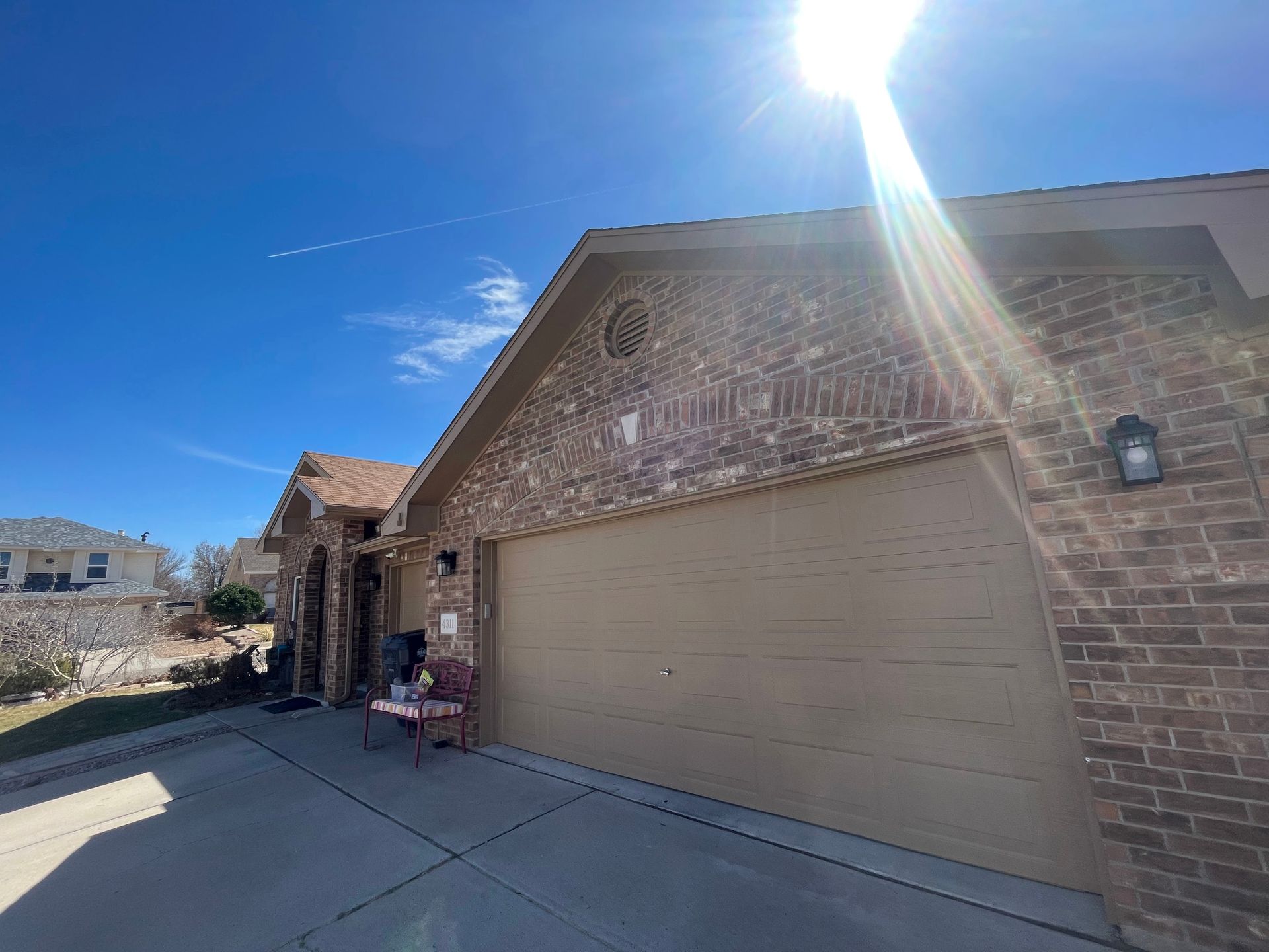 Brick house with beige garage door under bright sun, viewed from the driveway.