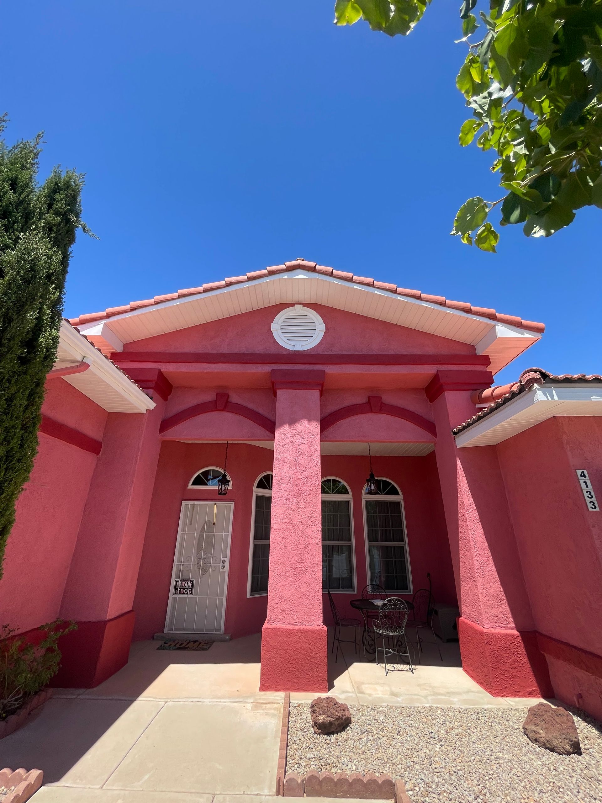 Pink stucco building entrance with a covered porch and tiled roof under a blue sky