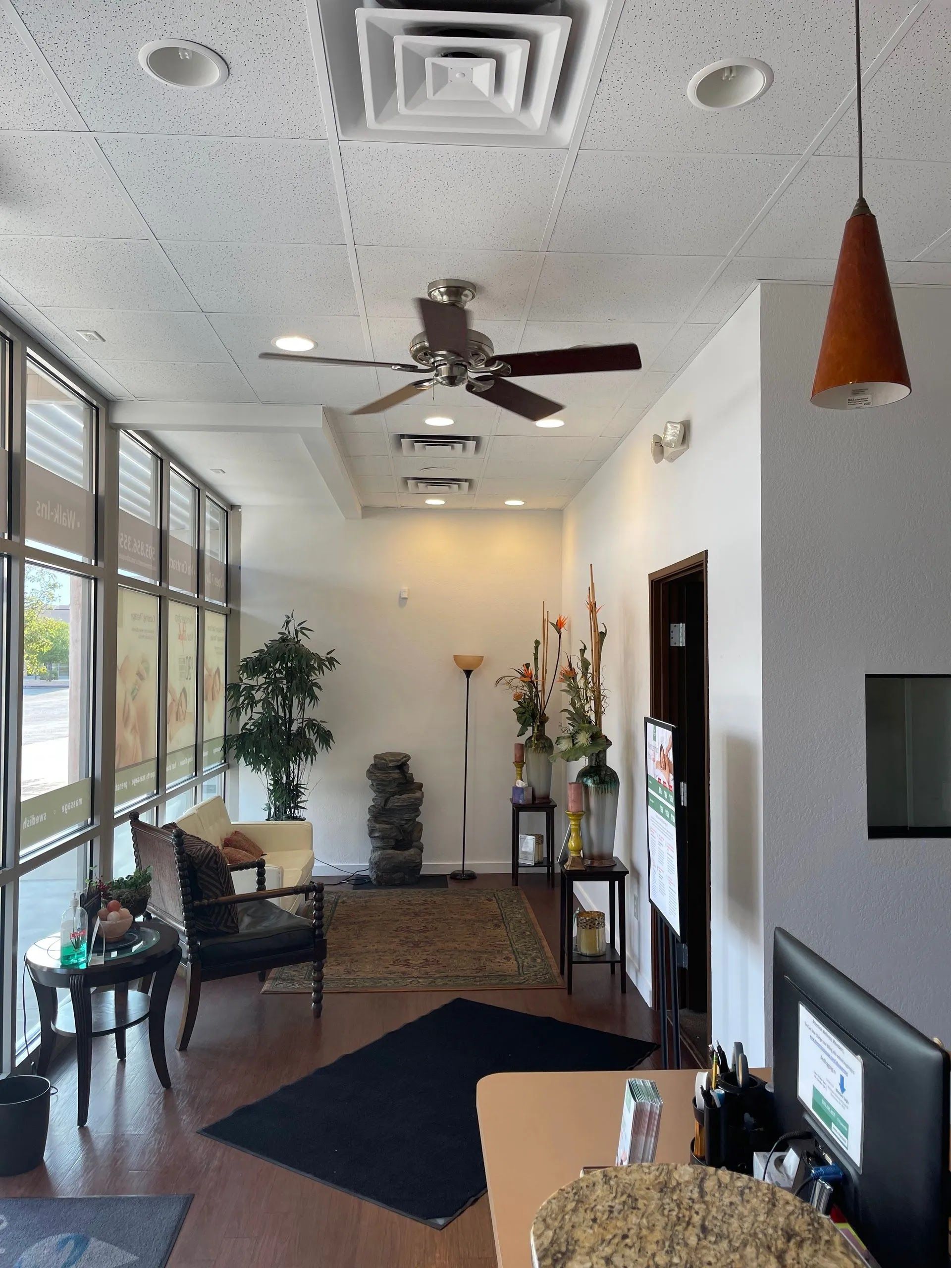 Bright lobby with large windows, ceiling fan, seating area, and front desk near potted plants