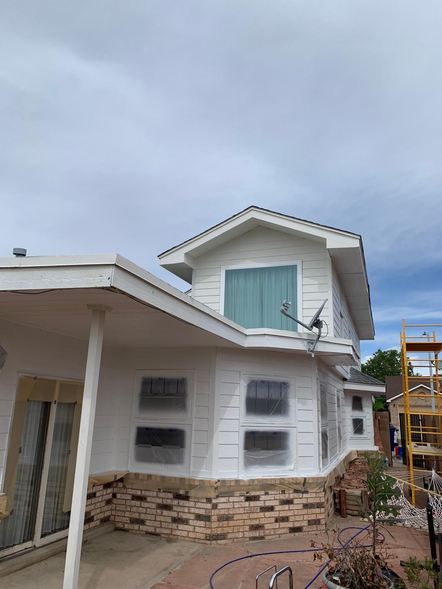White house exterior with stone base, blue shutters, and a cloudy sky