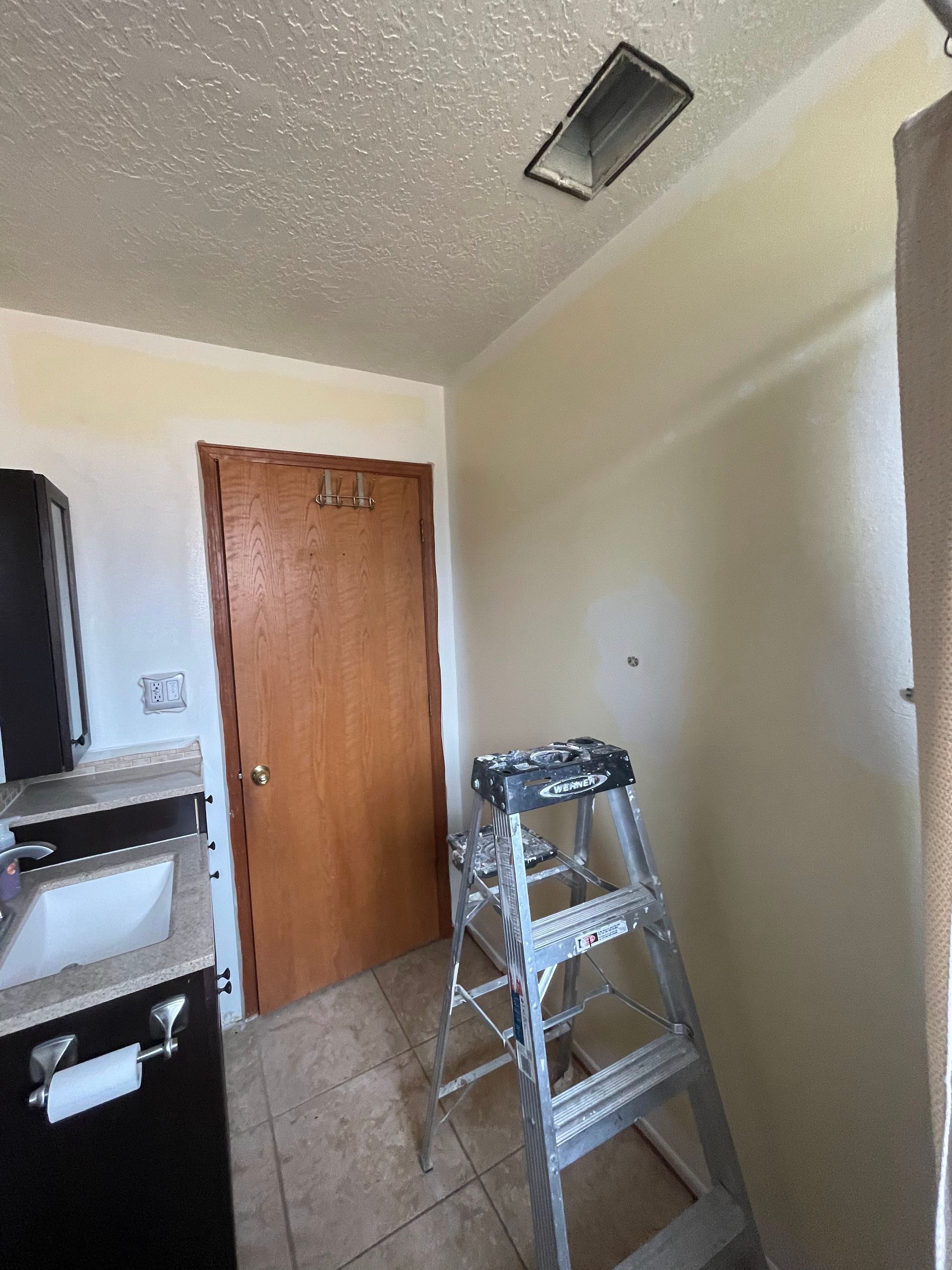 Small utility room with a wooden door, tiled floor, and a step ladder in the foreground.