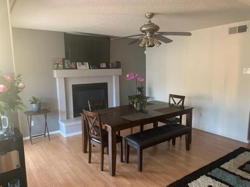 Dining room with dark wood table and bench, fireplace, ceiling fan, and potted orchid on the table.