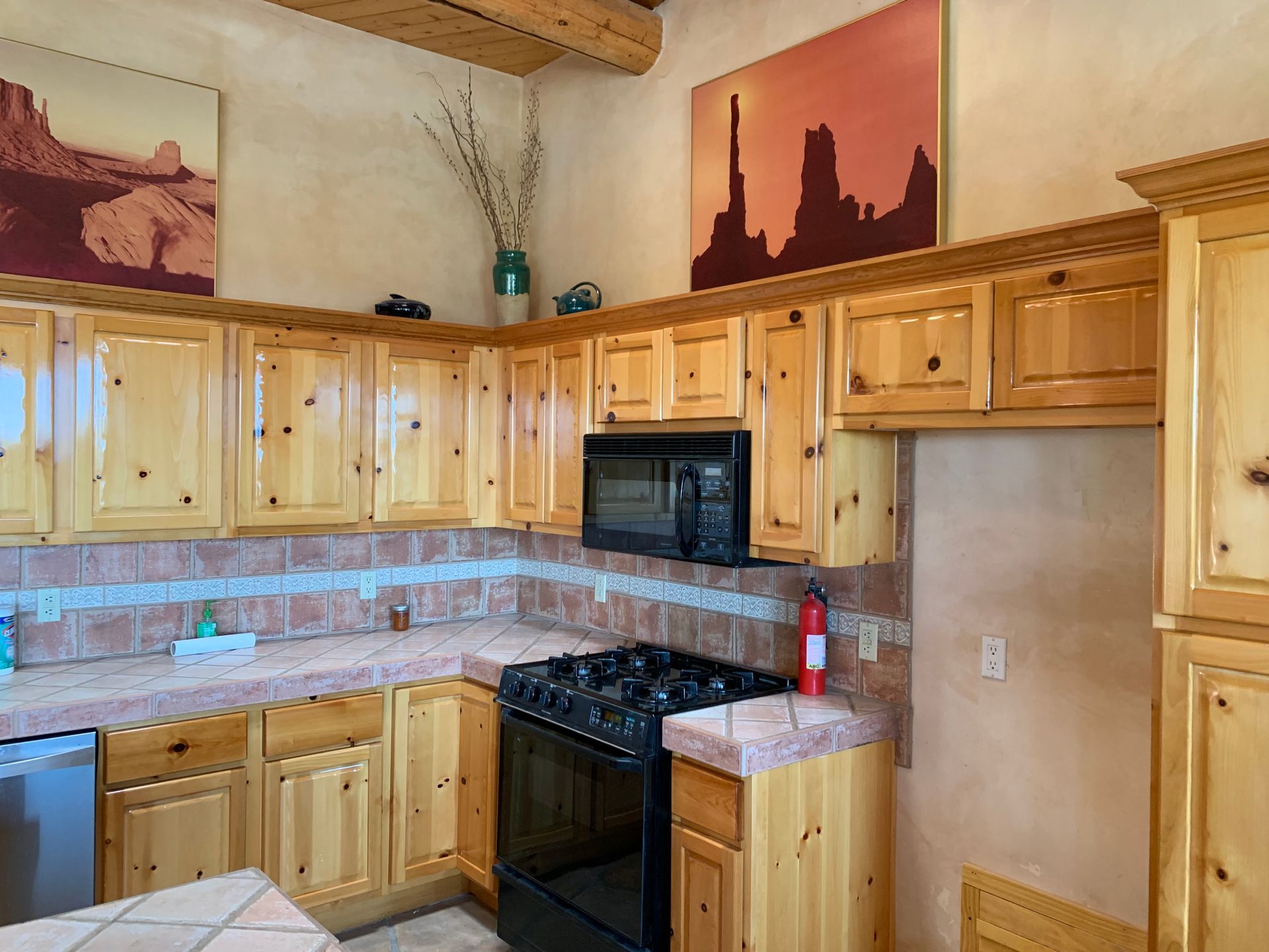 Wooden kitchen with black stove, microwave, tan tile backsplash, and desert artwork on the walls