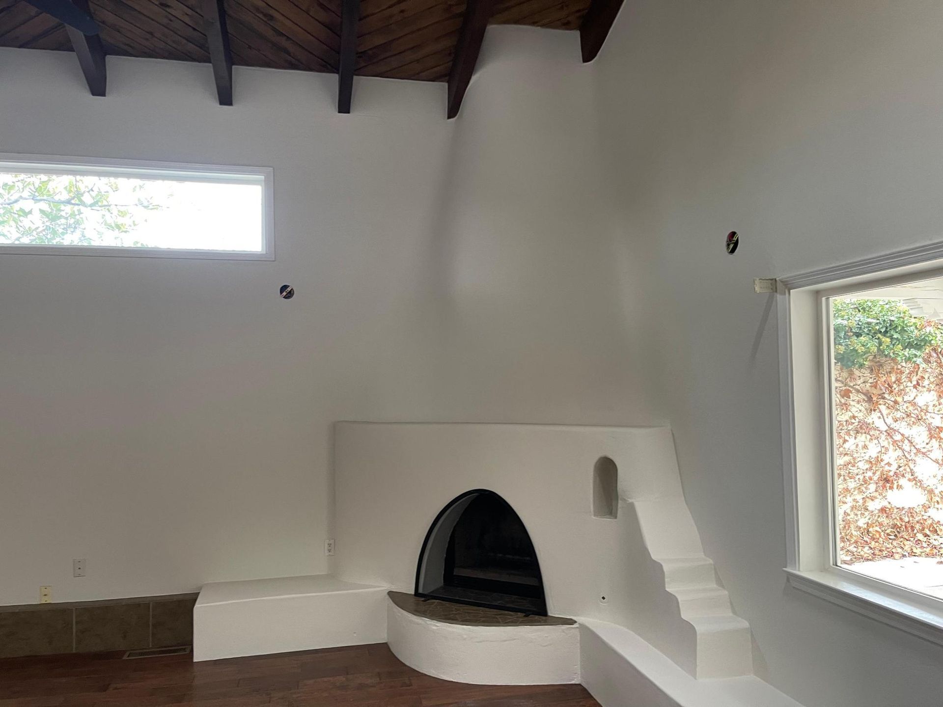 White room with a small arched fireplace, high ceiling, and two windows letting in natural light