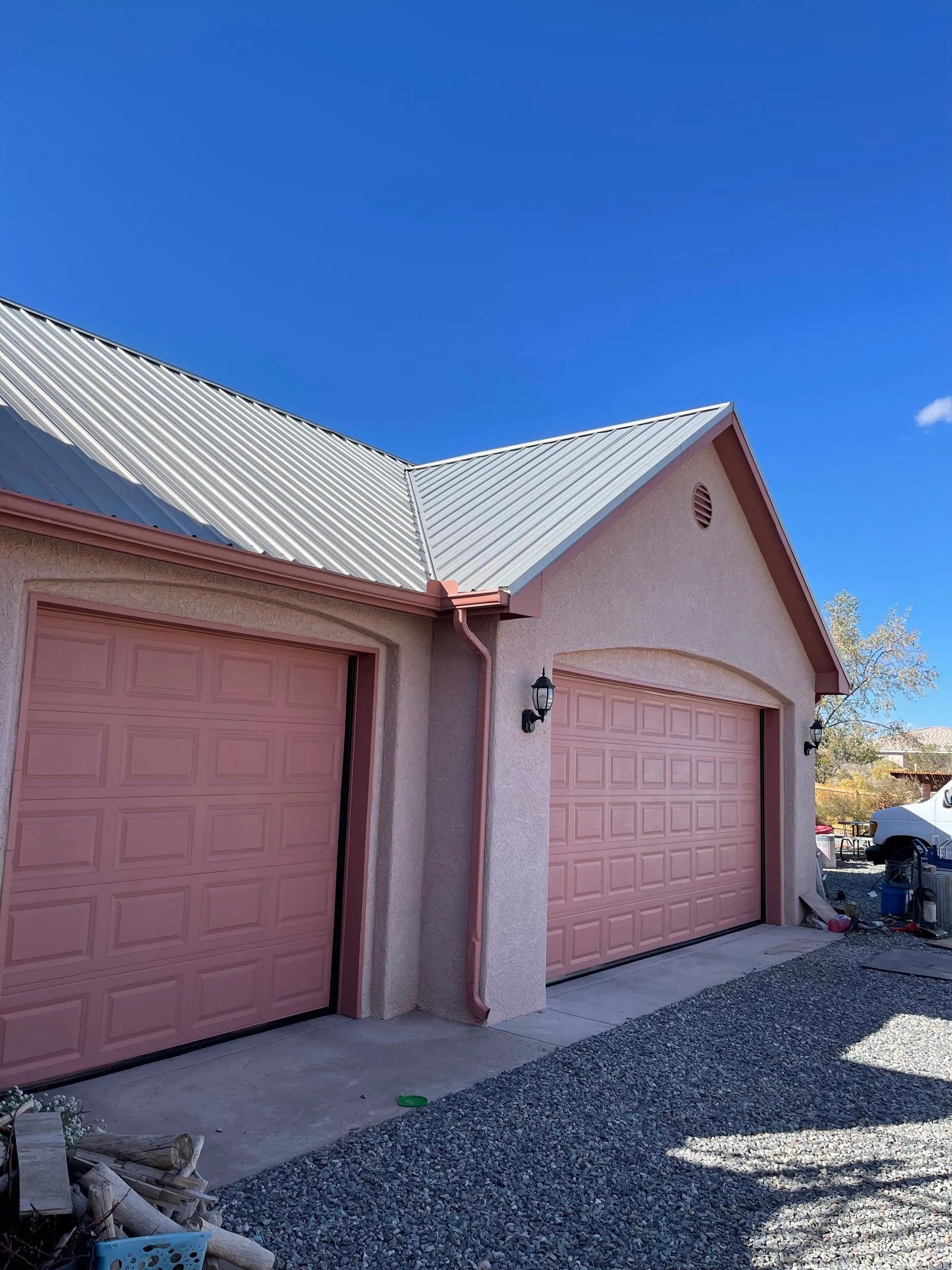 Pink garage doors on a stucco house with a gray roof and gravel driveway under a blue sky