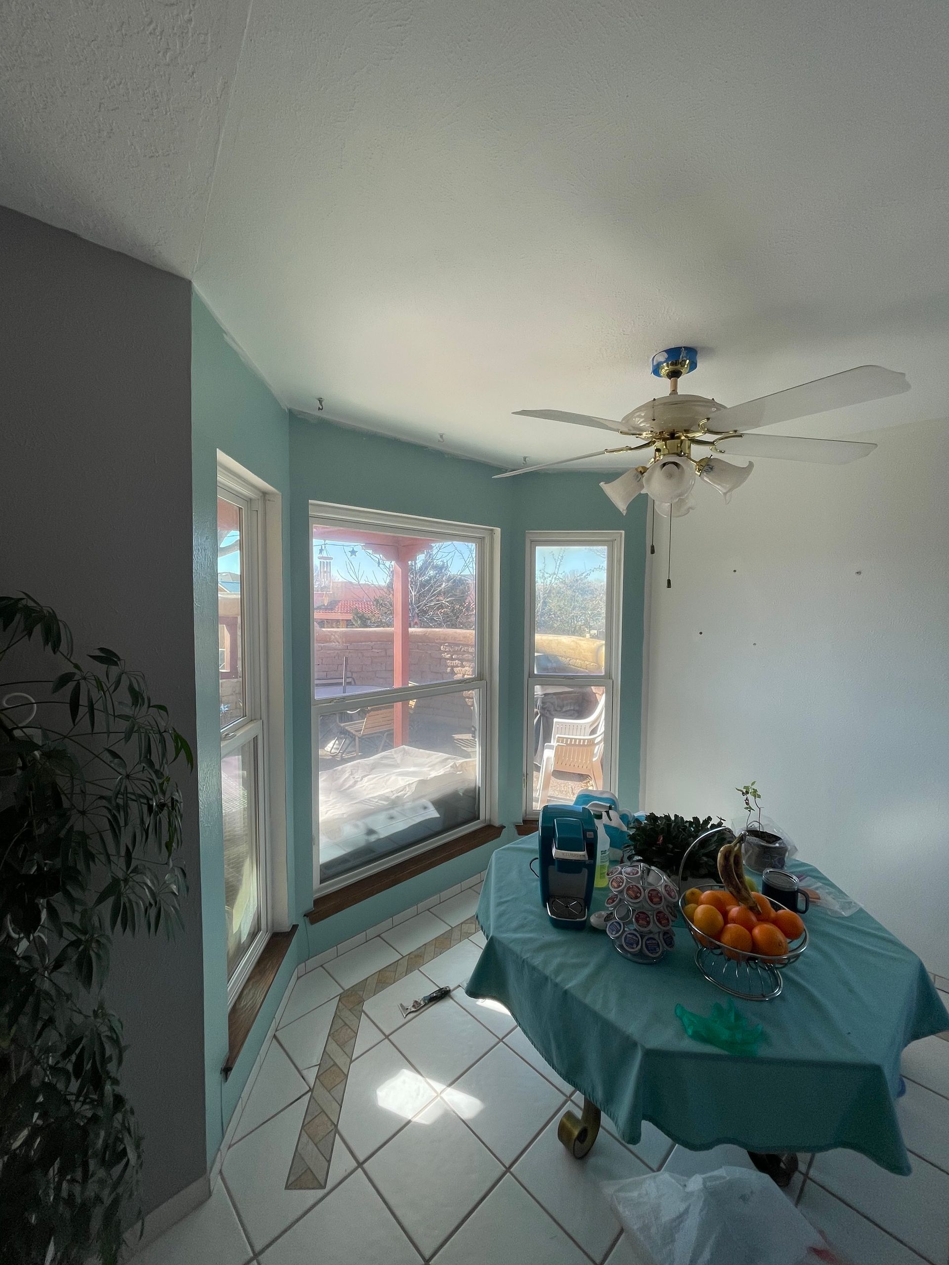 Dining nook with round table, teal tablecloth, fruit, and bay windows filling the room with sunlight