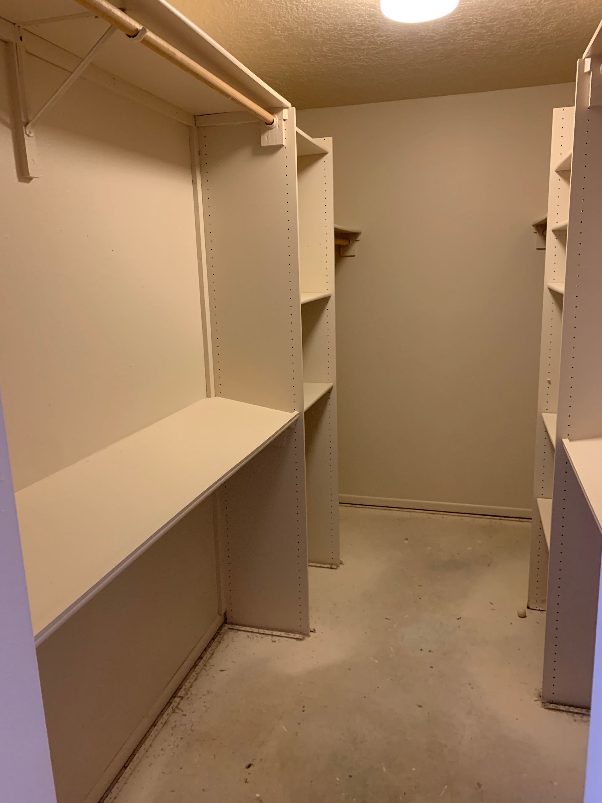 Empty walk-in closet with white shelves, hanging rods, and beige carpet under a ceiling light.