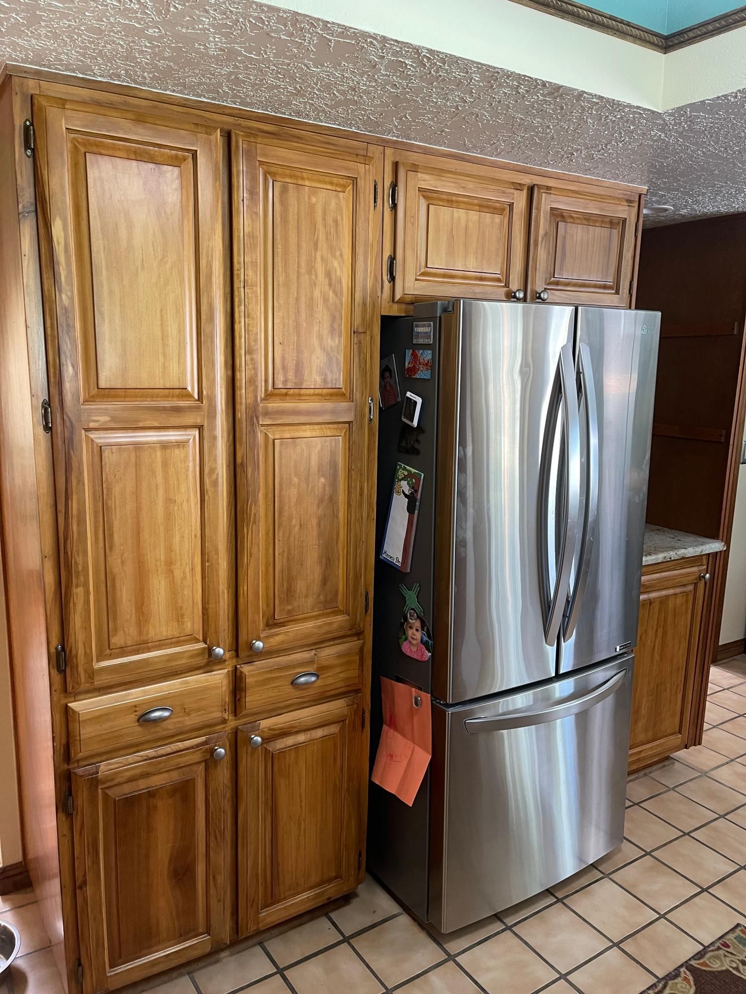 Kitchen with wooden cabinets and a stainless steel refrigerator on a tiled floor.
