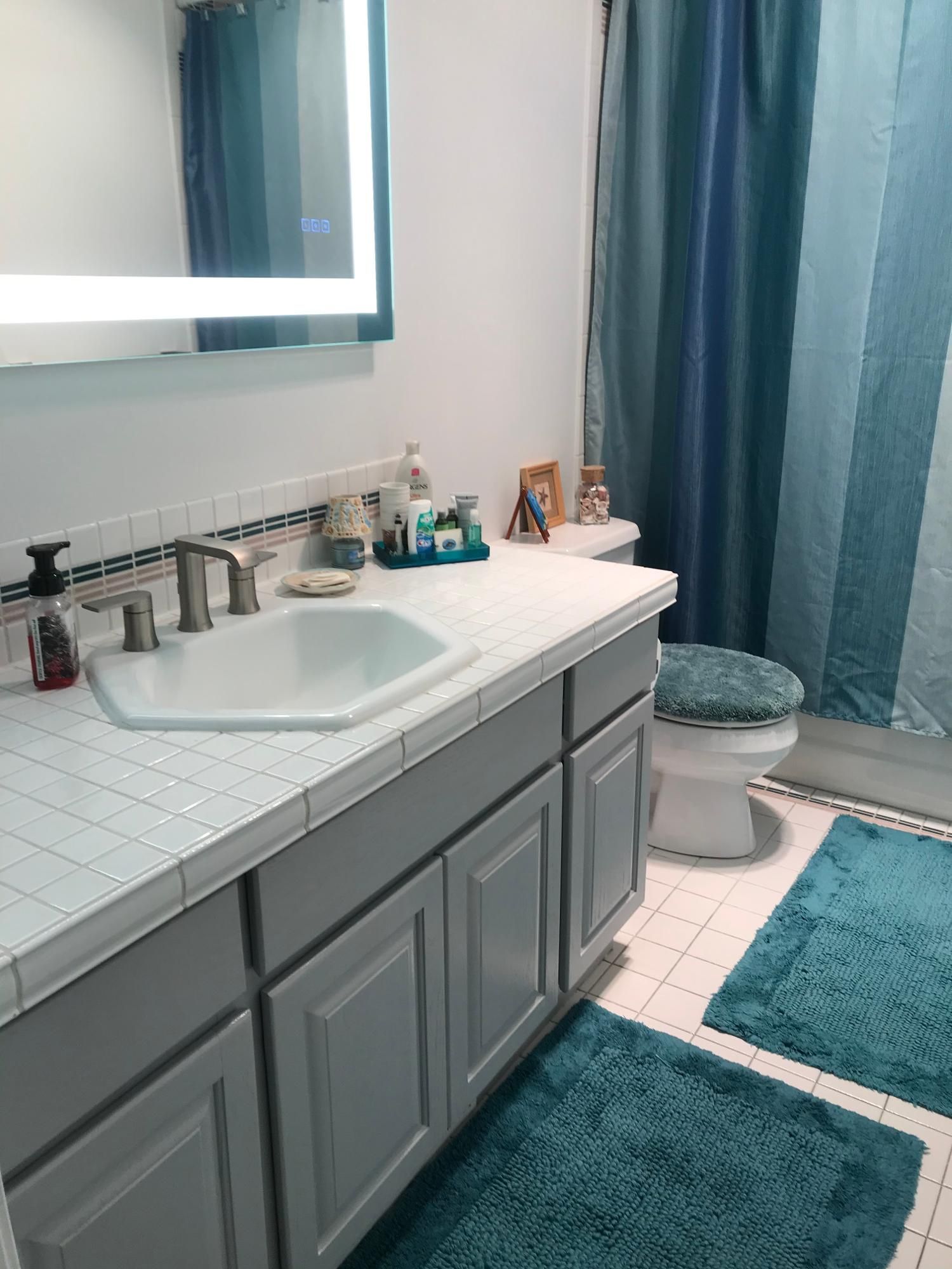 Bathroom vanity with white sink, gray cabinets, teal rug, and blue shower curtain