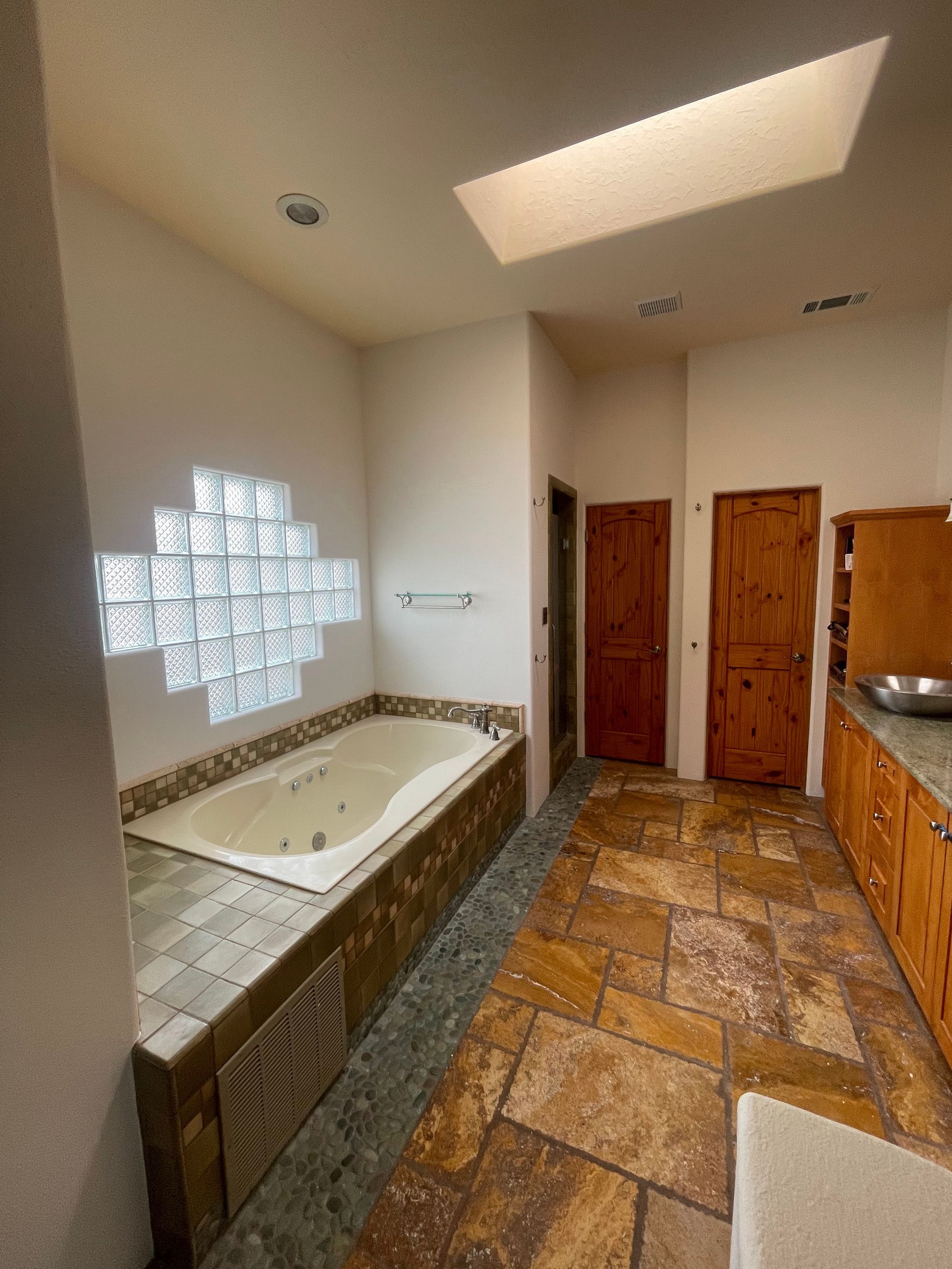 Bathroom with a tiled tub alcove, glass-block window, skylight, and wood doors over patterned floor tiles