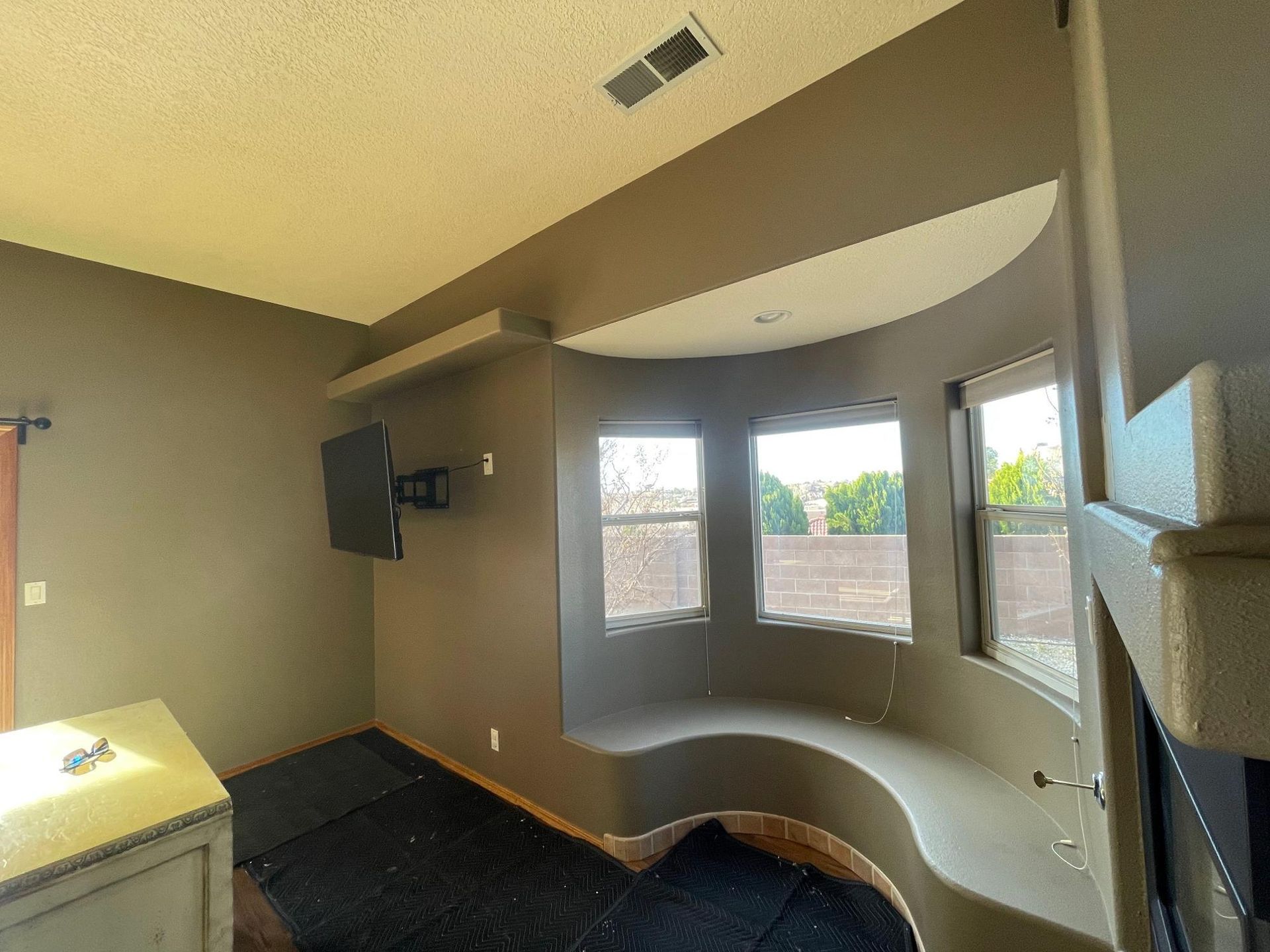 Empty living room with curved built-in bench, wall-mounted TV, and large windows.