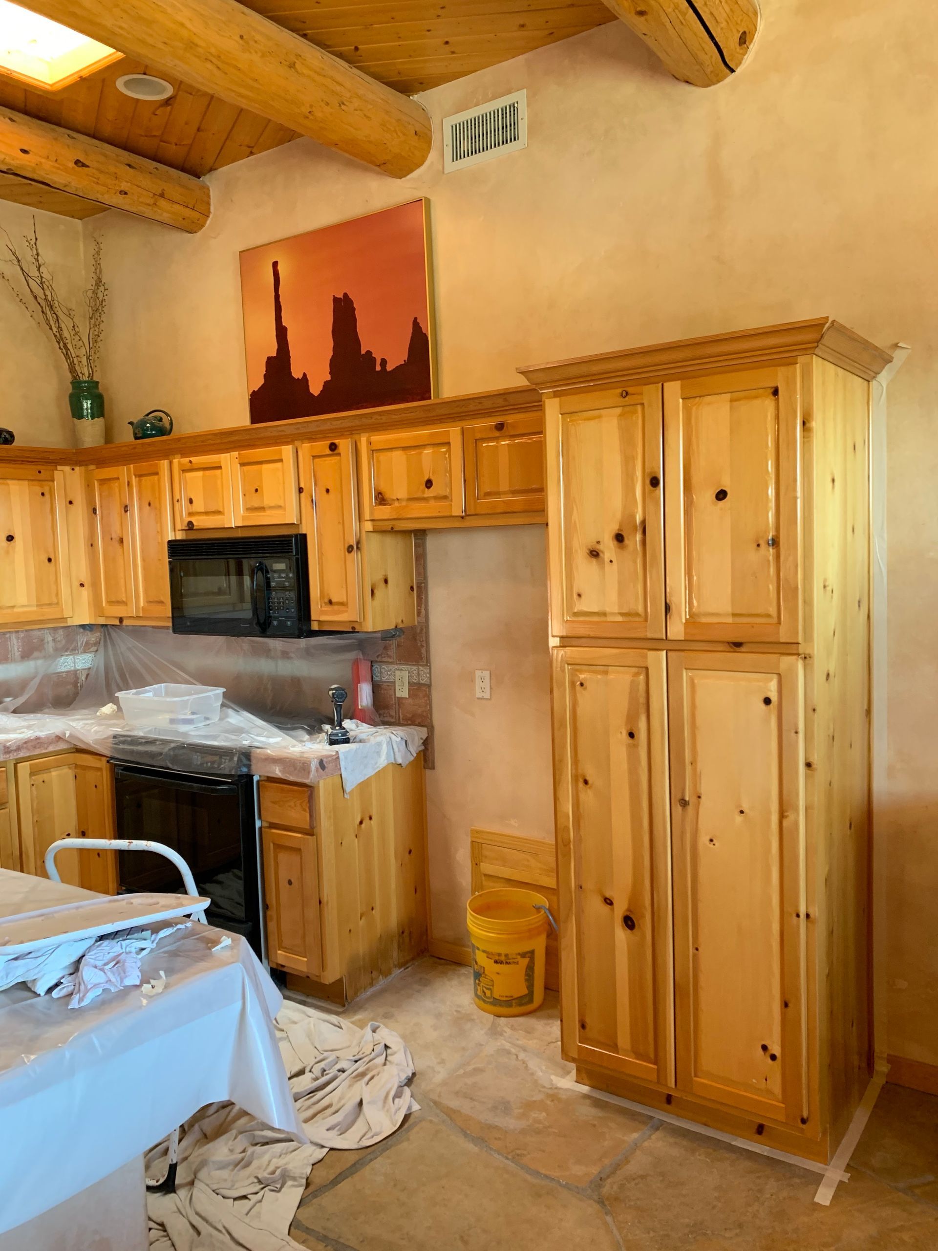 Wood-paneled kitchen with wooden cabinets, vaulted ceiling, and a table covered in plastic sheeting.