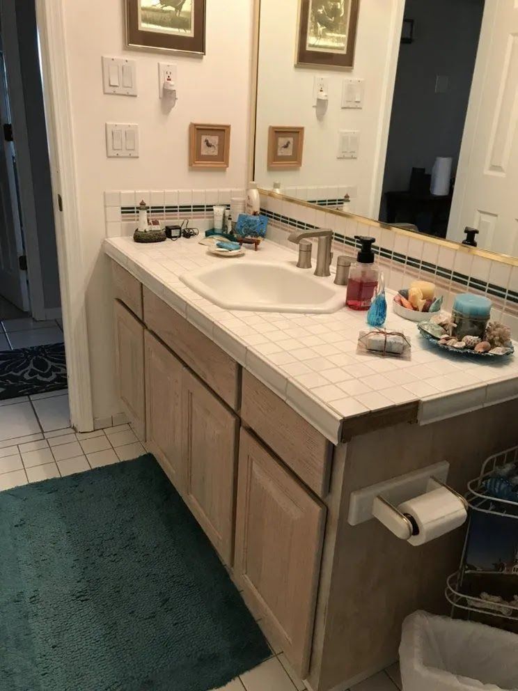 Bathroom vanity with mirror, white countertop, beige cabinets, and toiletries on the counter