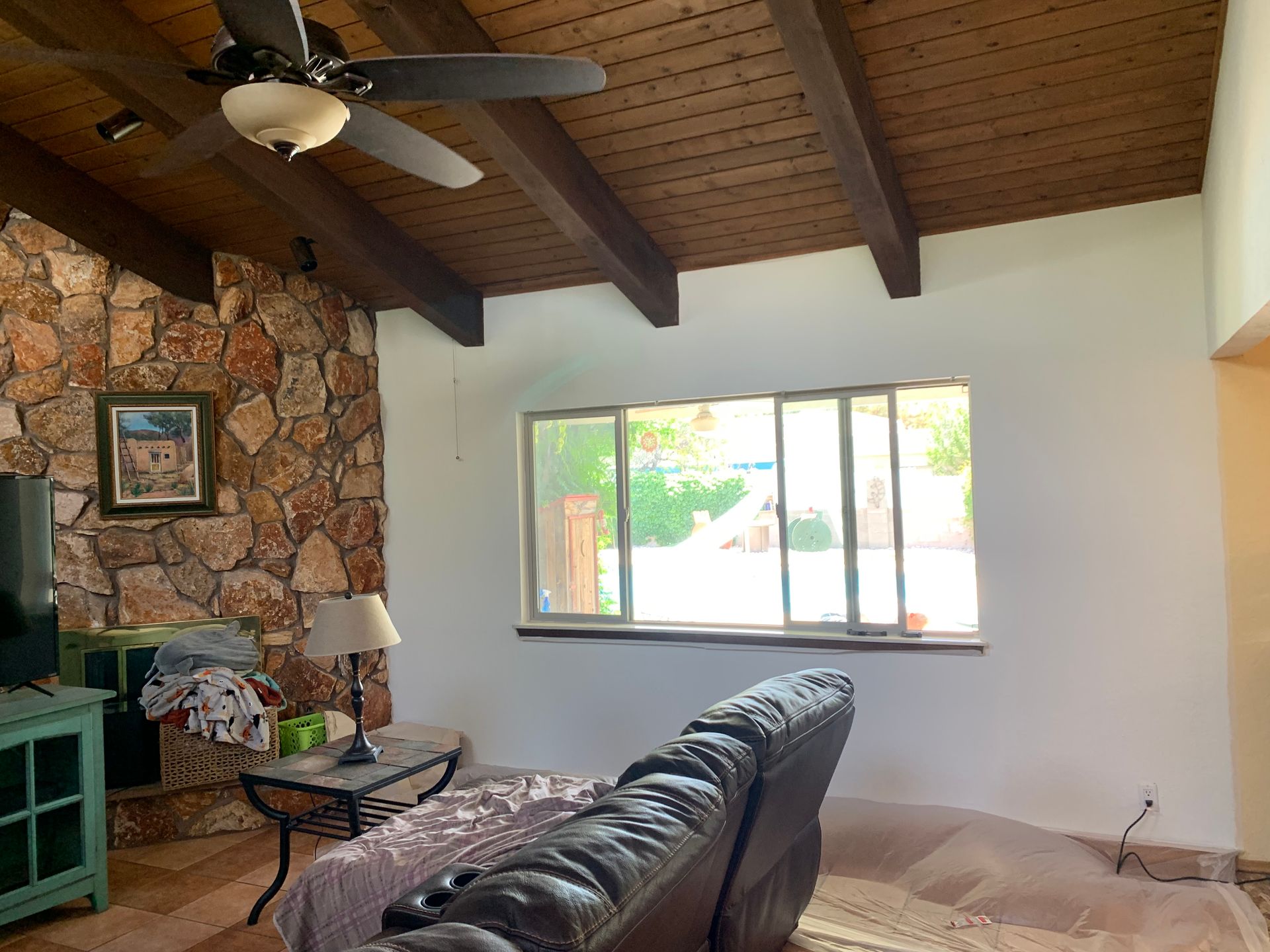 Living room with stone fireplace, ceiling fan, sofa, and large window with bright outdoor light