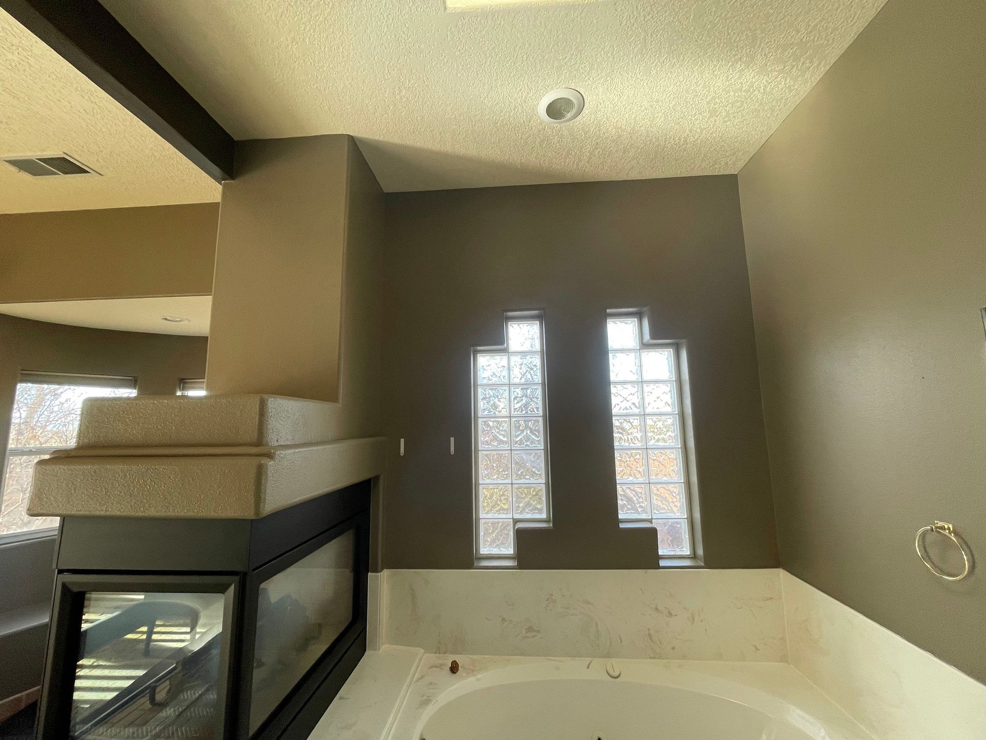 Modern bathroom with beige walls, freestanding tub, glass shower, and tall windows letting in daylight