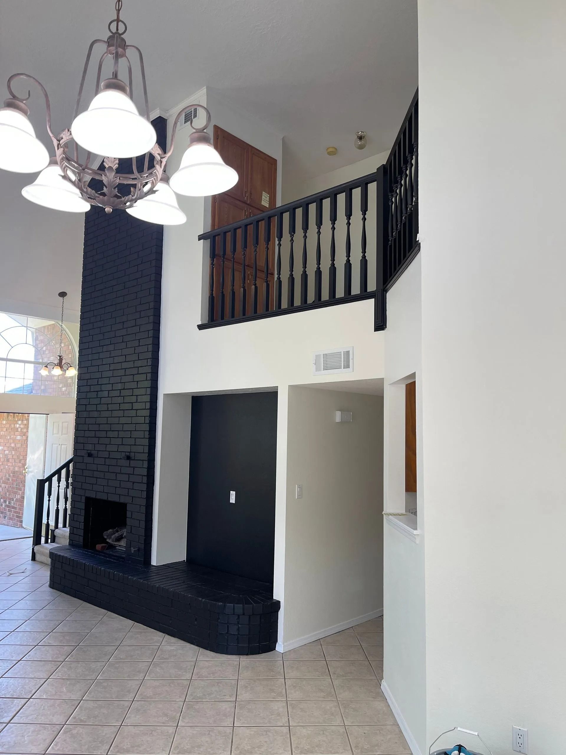 Modern foyer with tiled floor, black accent wall, staircase railing, and chandelier lighting