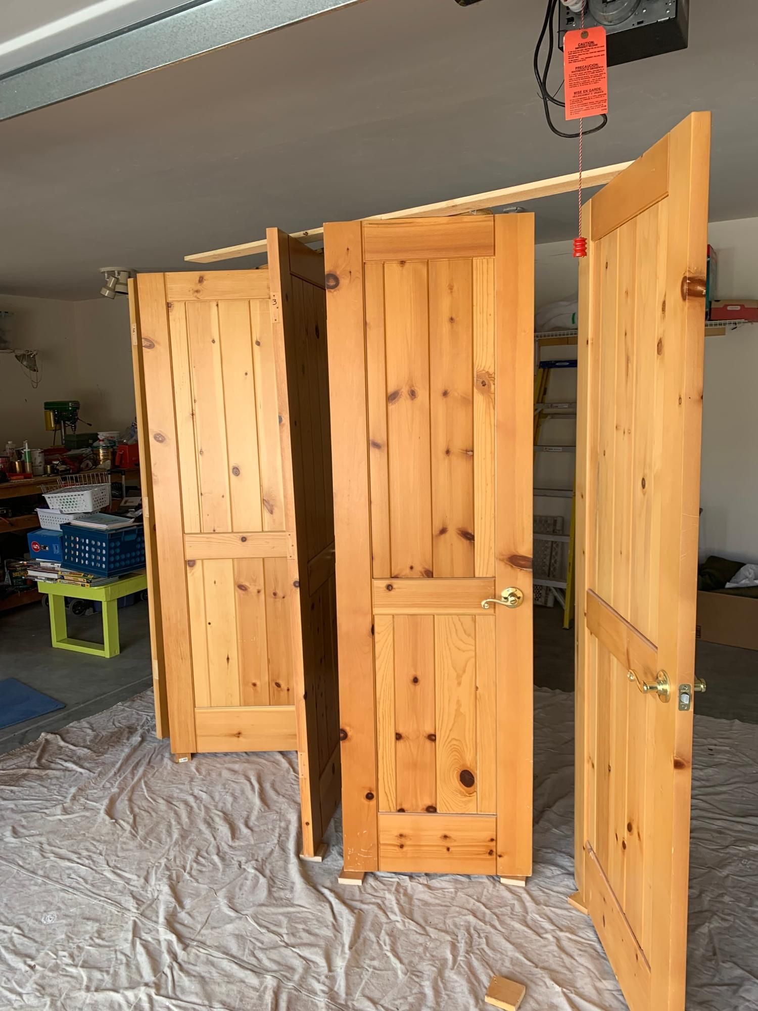 Three wooden doors leaning open in a garage, with a white drop cloth on the floor