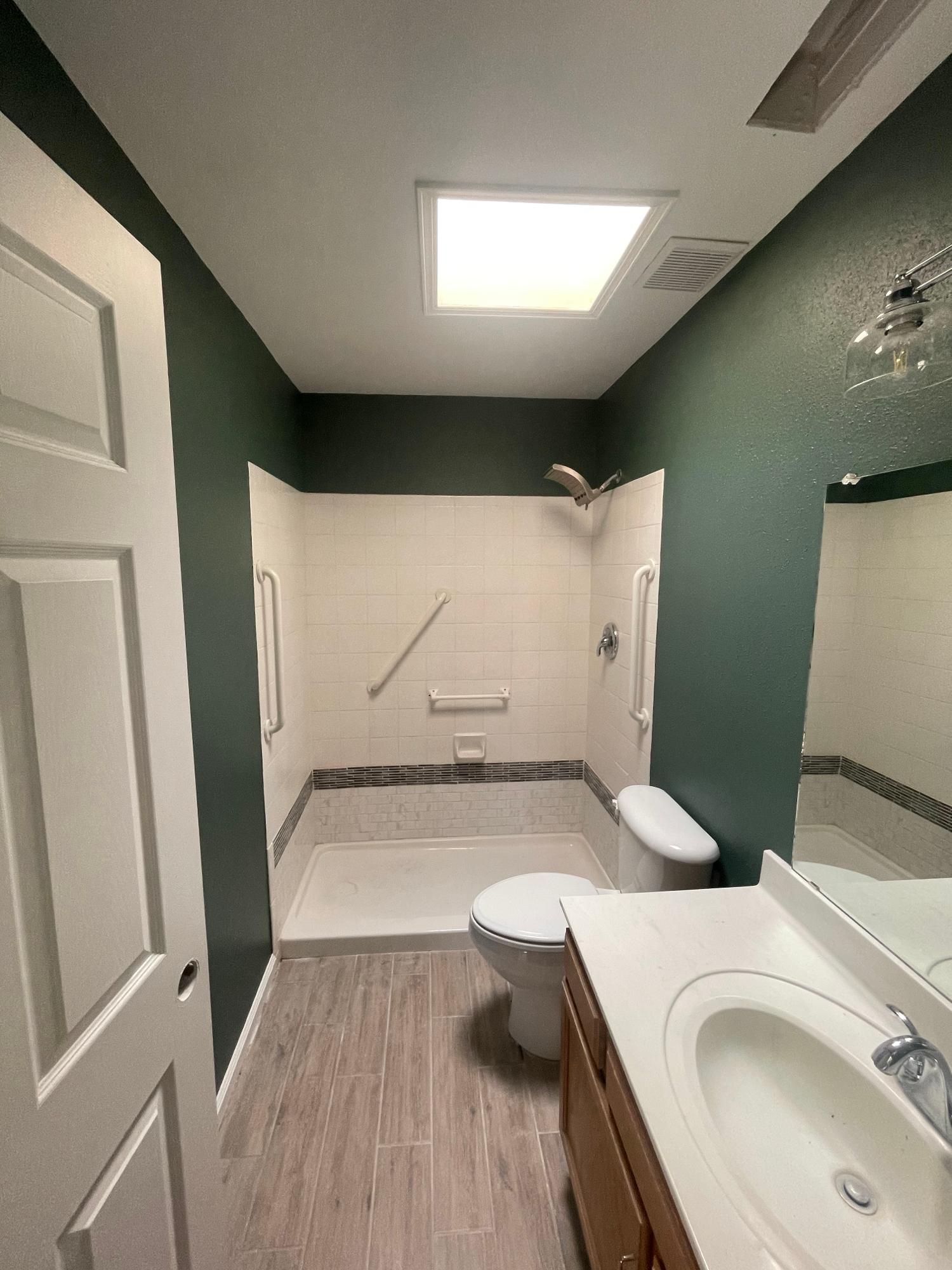 Bathroom with green walls, white tub shower, and sink under a bright ceiling light.