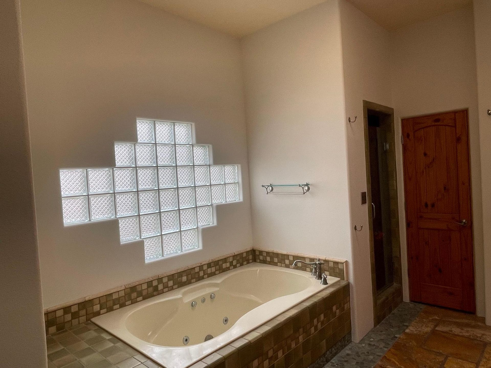 Bathroom with a corner soaking tub, glass block window, beige walls, and wood door.