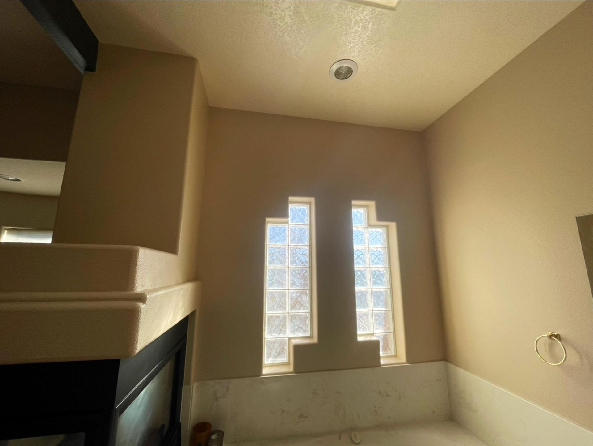 Small bathroom with beige walls, two narrow frosted windows, and a bathtub under the windows.