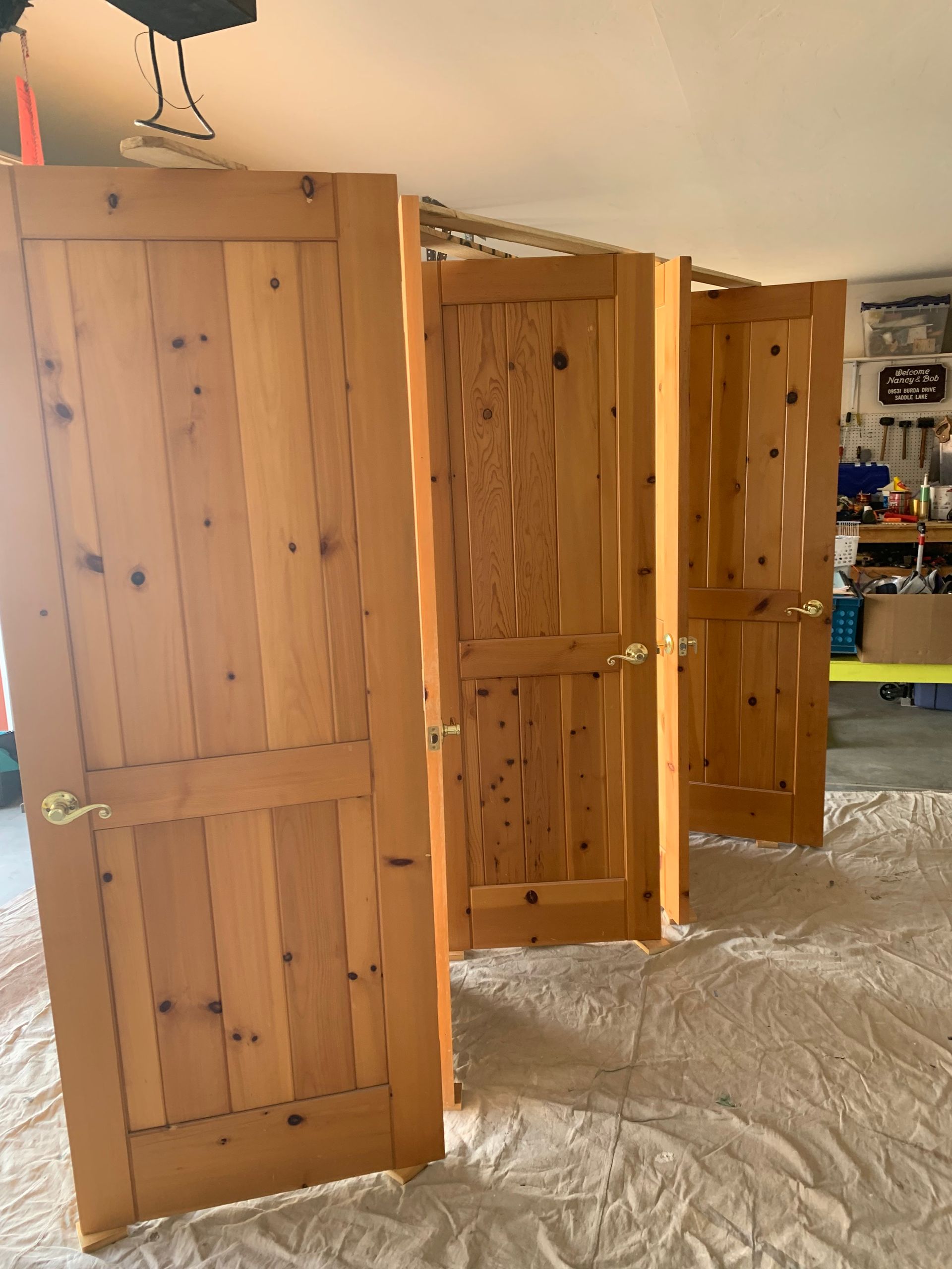 Three wooden doors propped open in a room under renovation, with plastic sheeting on the floor.
