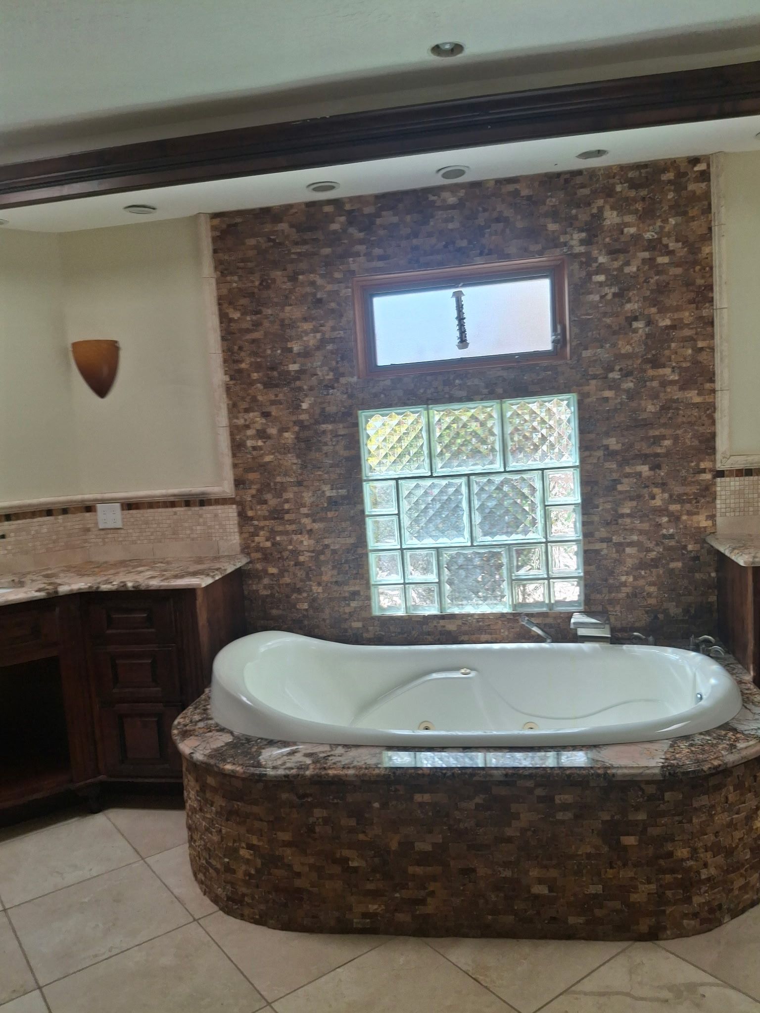 Bathroom with a white bathtub set into a stone surround beneath a frosted glass window.