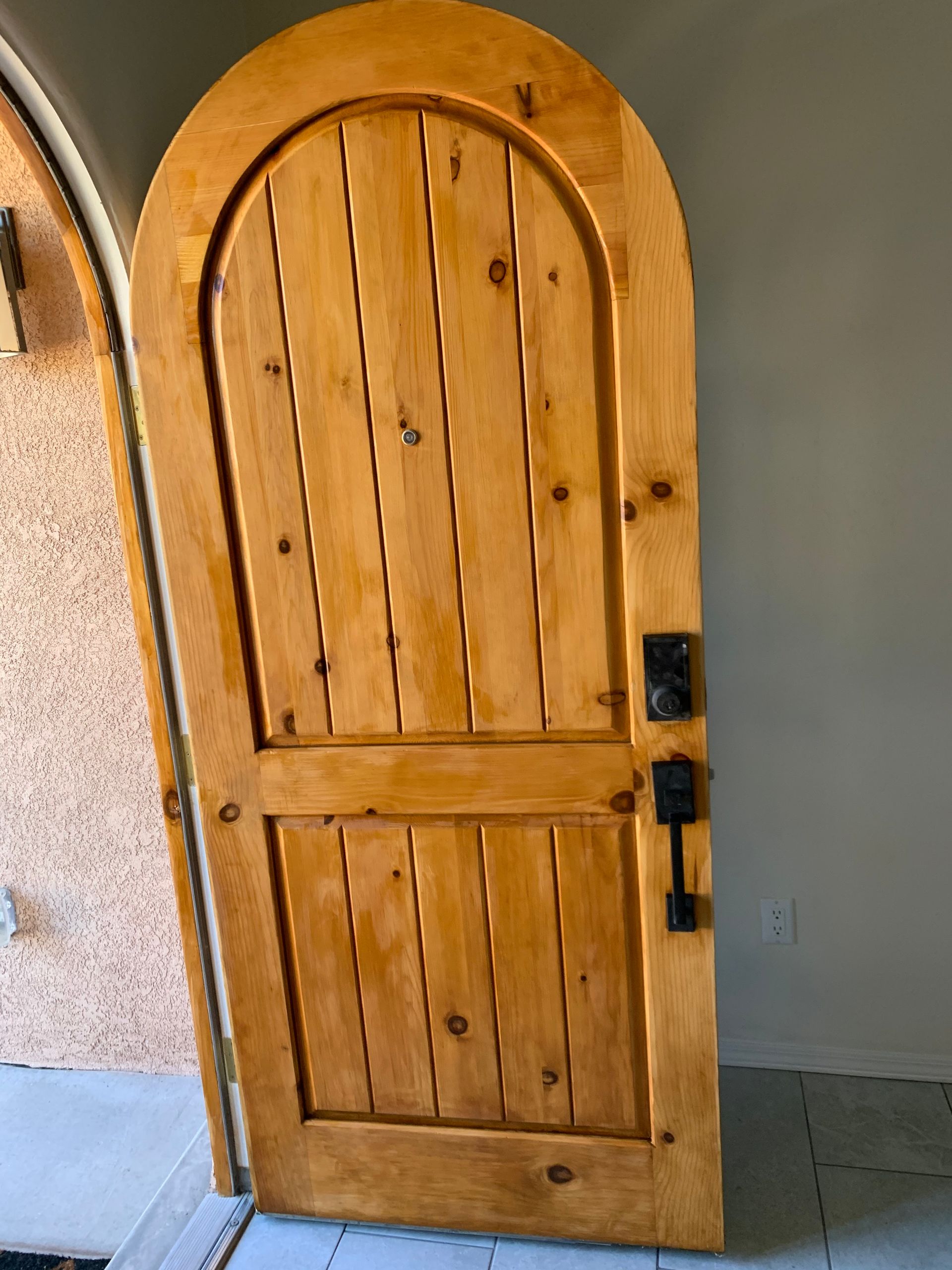 Wooden arched door with black handle and lock in a gray-walled entryway