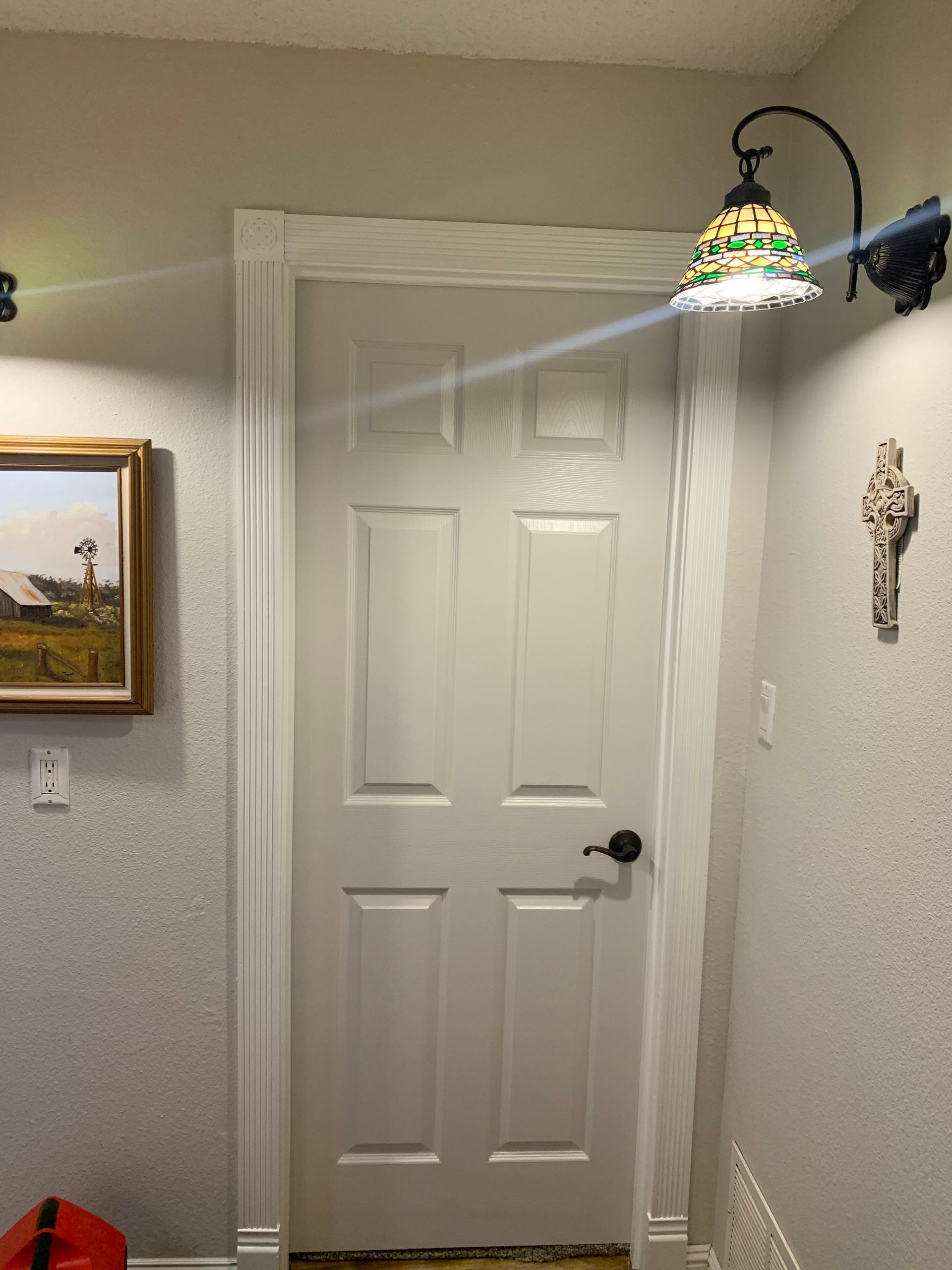 Interior hallway with a white paneled door, framed painting, wall sconce, and stained-glass pendant light.