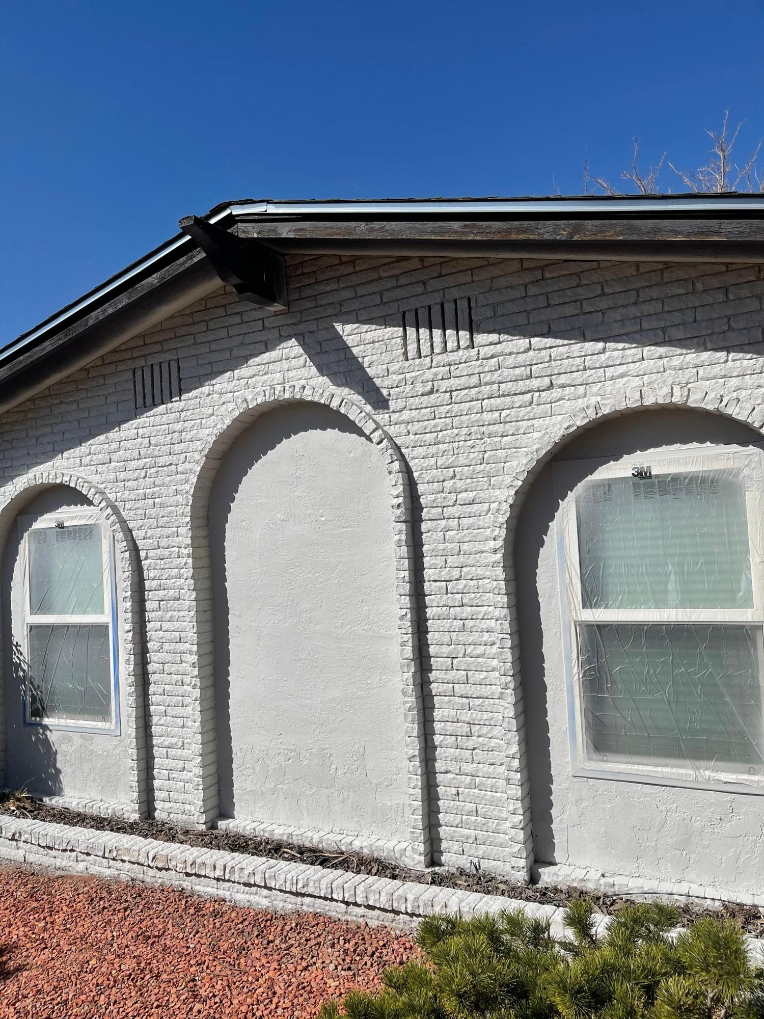 Exterior of a white stucco house with arched window frames and a blue sky above
