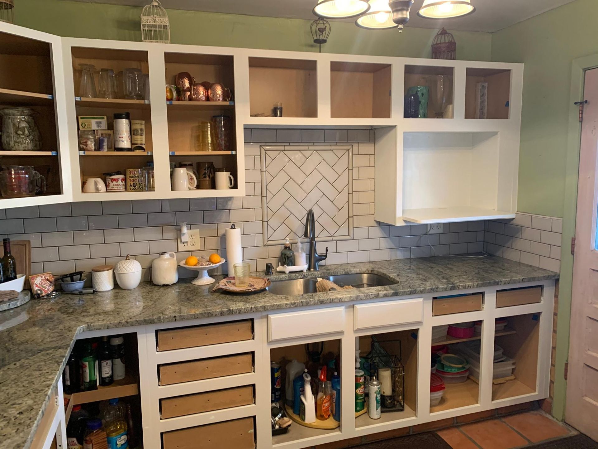 Kitchen with open cabinets, white subway tile backsplash, green walls, and gray countertop.