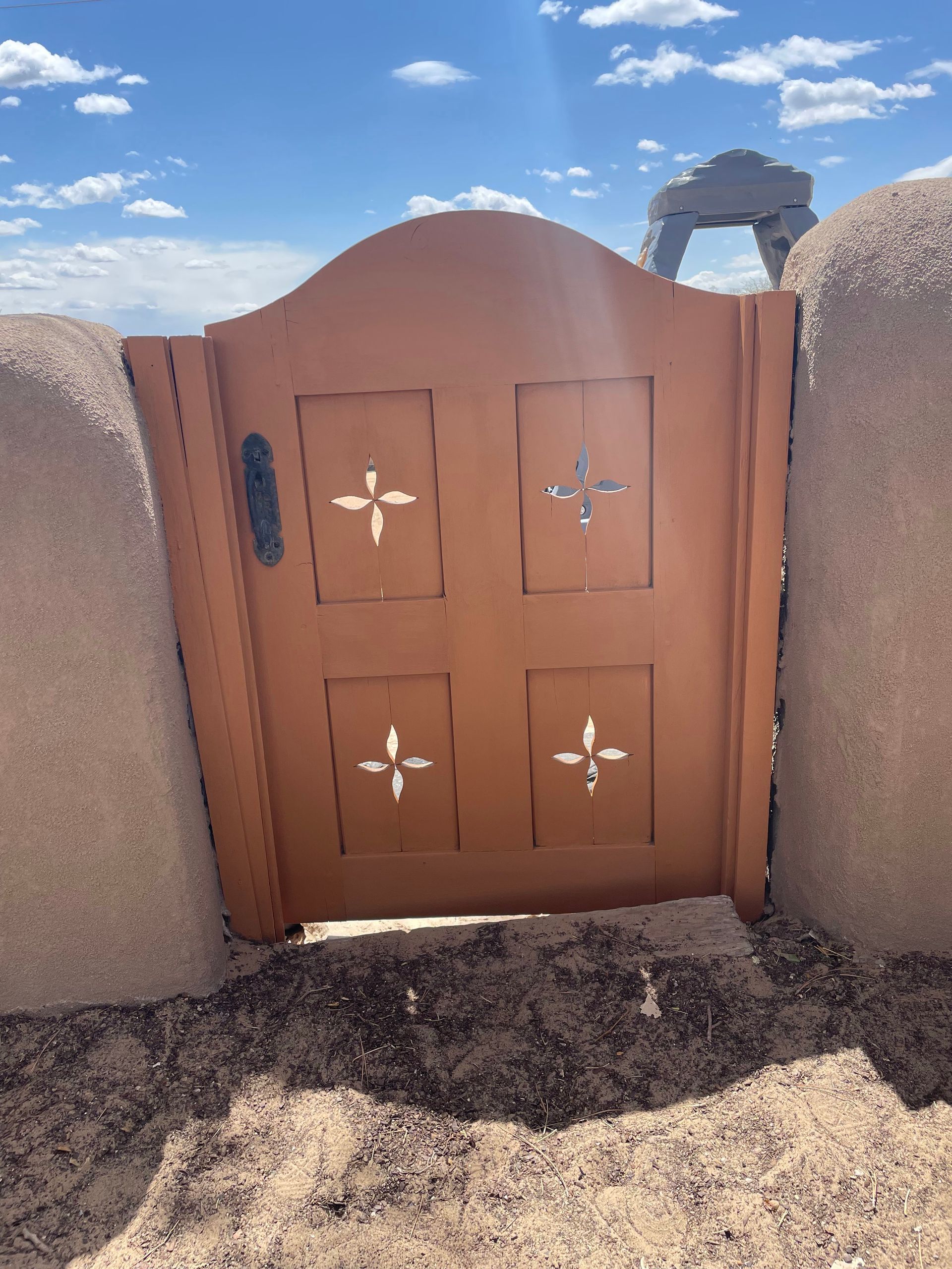 Tan gate with cutout cross designs set in a stucco wall under a blue sky.