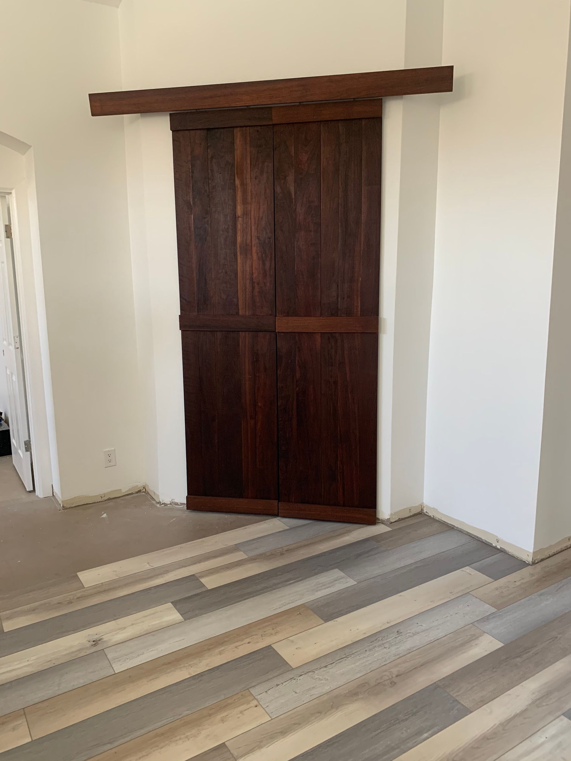 Closed dark wood sliding door in a white room with patterned wood-look flooring.