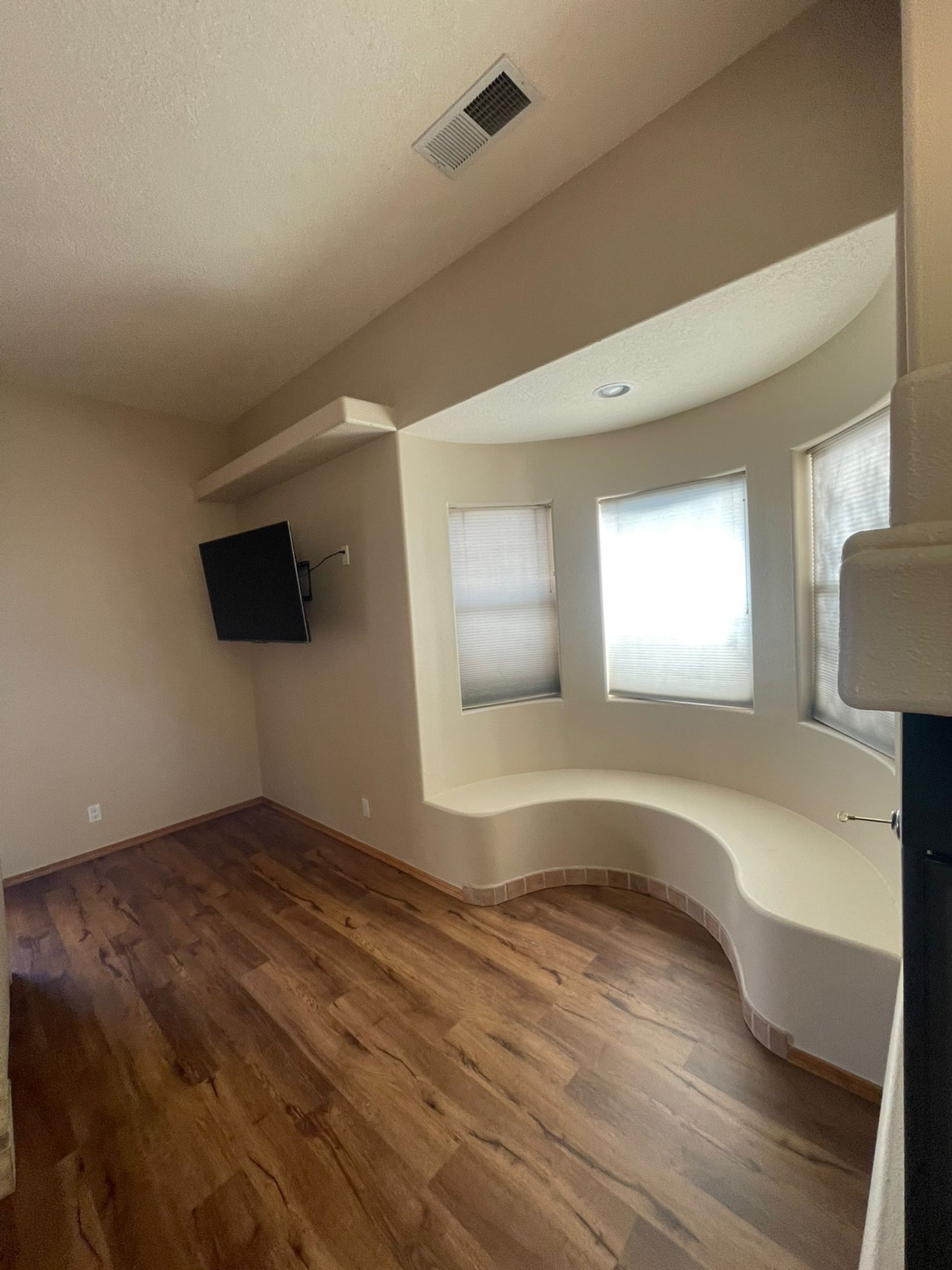 Empty living room with curved bay window seating, hardwood floor, and wall-mounted TV