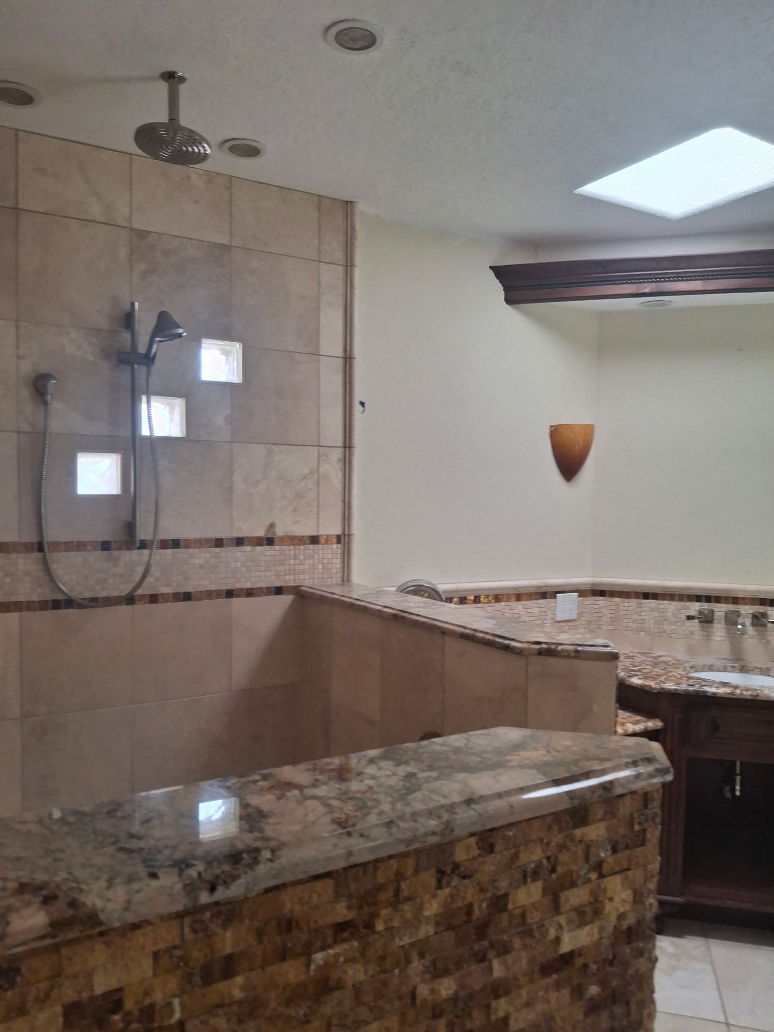 Bathroom with granite tub surround, tiled shower, and wall-mounted showerhead under a skylight.