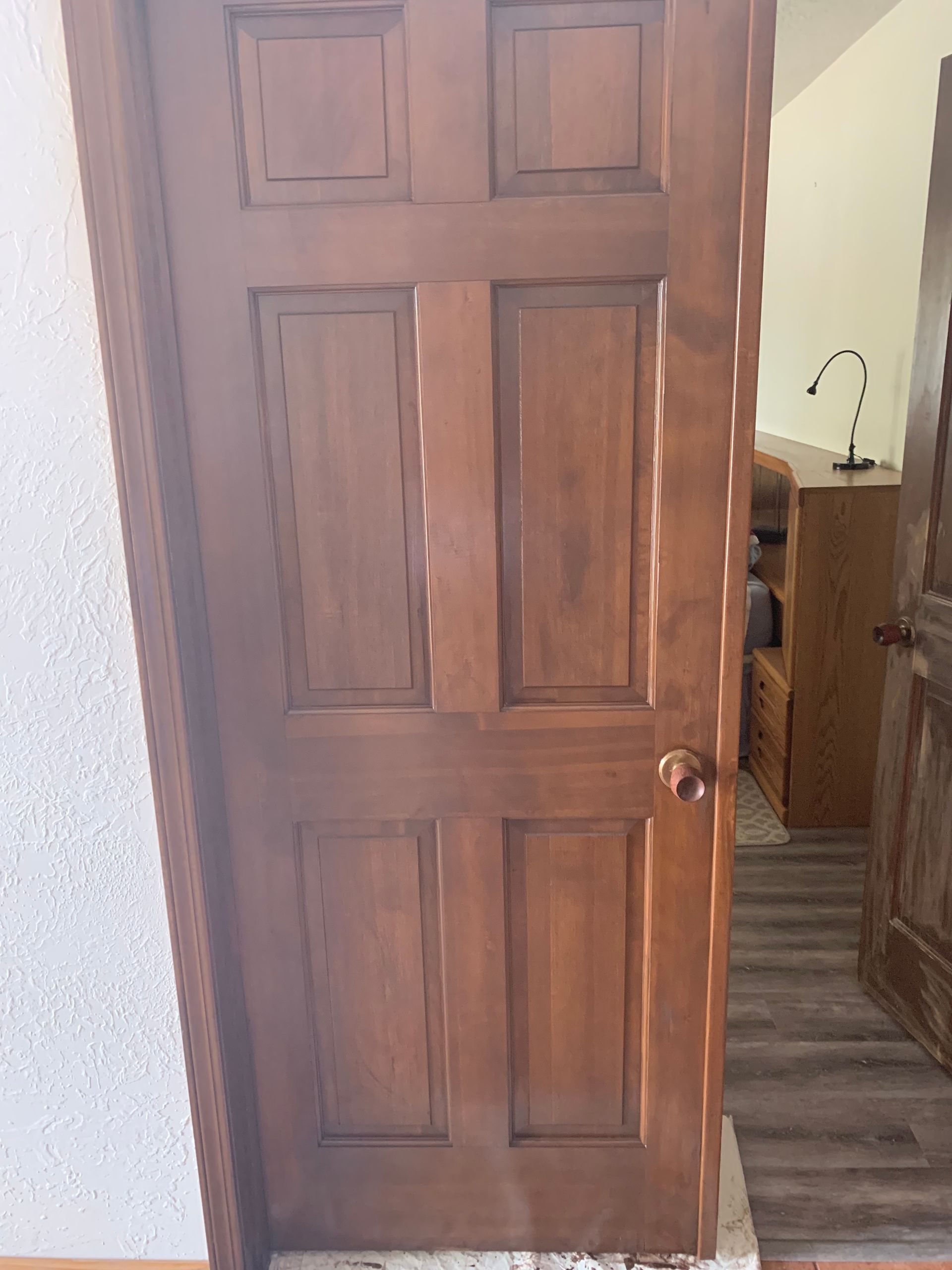 Wooden paneled door slightly open to a hallway with a glimpse of a kitchen sink.