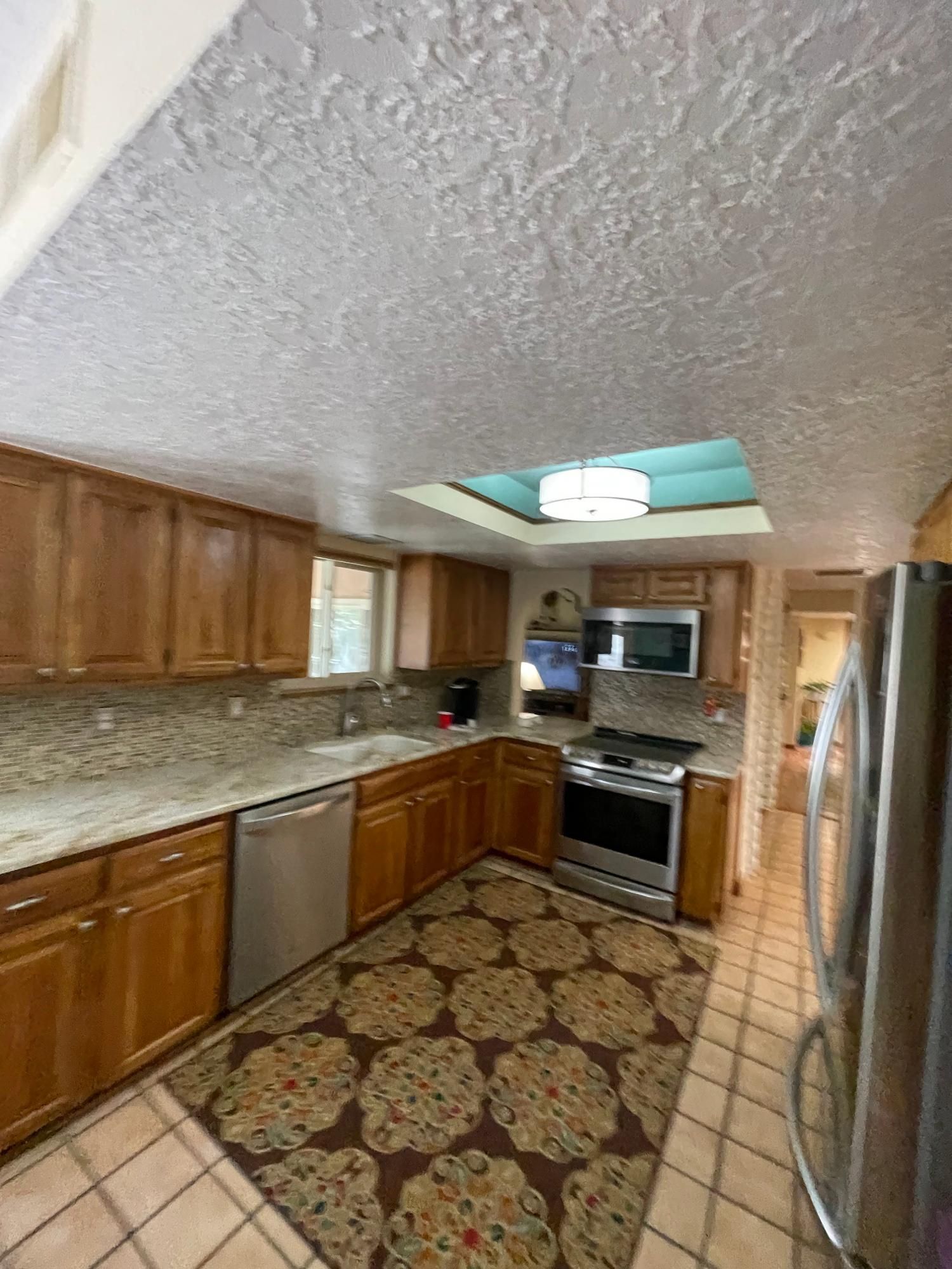 Narrow galley kitchen with wood cabinets, patterned floor, stainless appliances, and skylight ceiling.