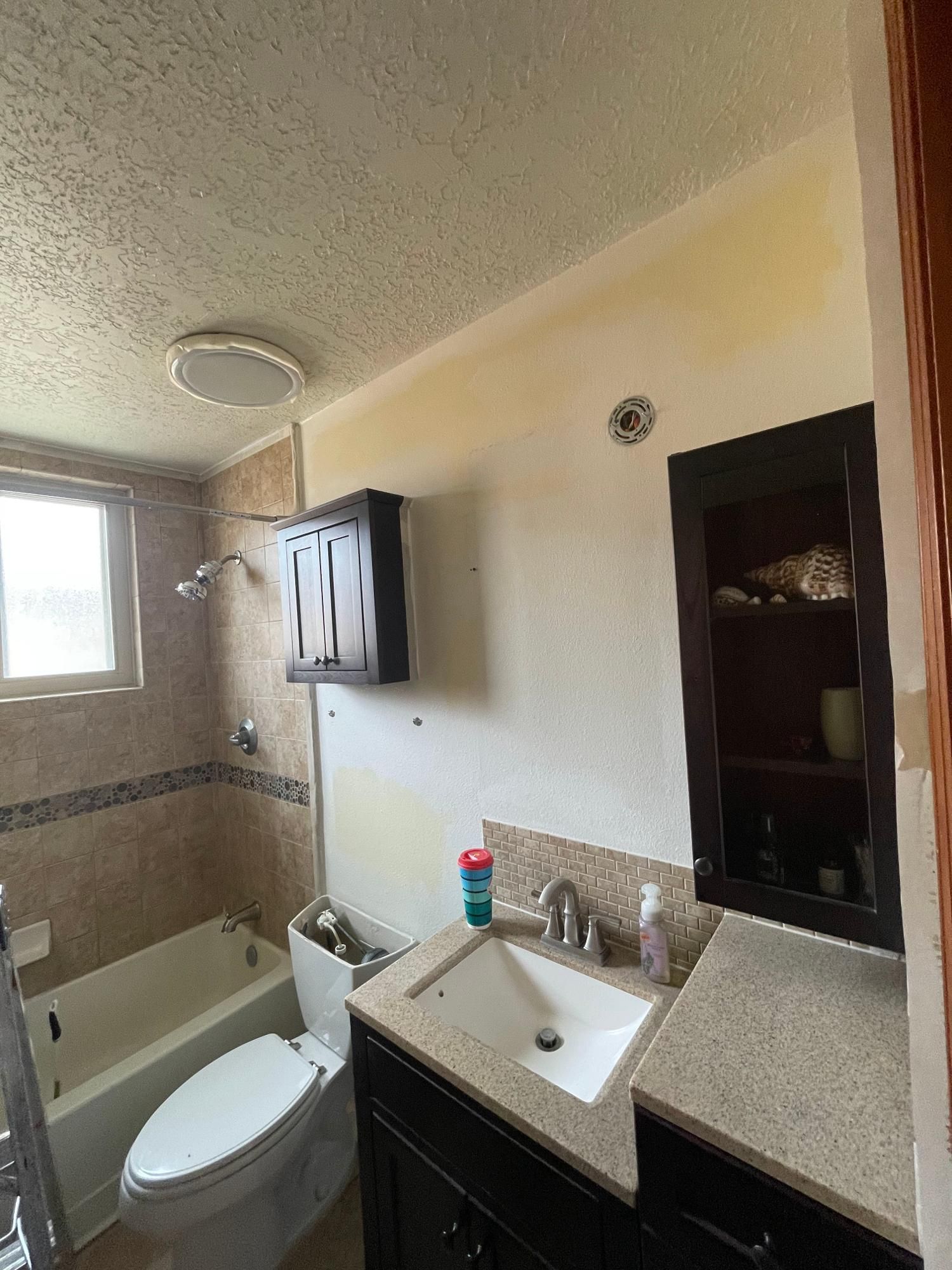 Small bathroom with toilet, bathtub, sink, dark vanity, and wall cabinet in beige tones
