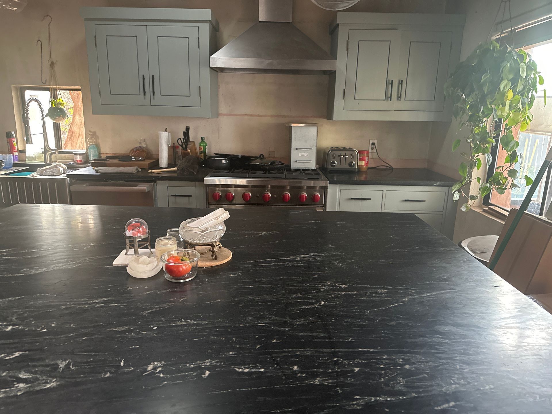 Modern kitchen with gray cabinets, black island countertop, red stove knobs, and potted plants near a window