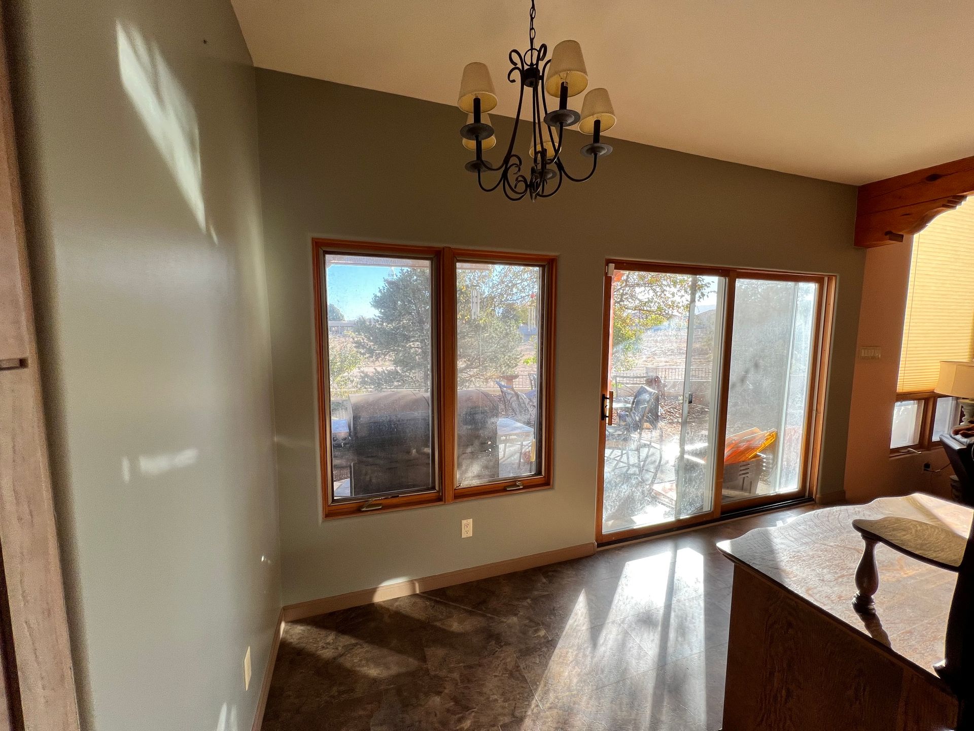 Empty dining room with large windows, chandelier, and sunlight on carpeted floor.