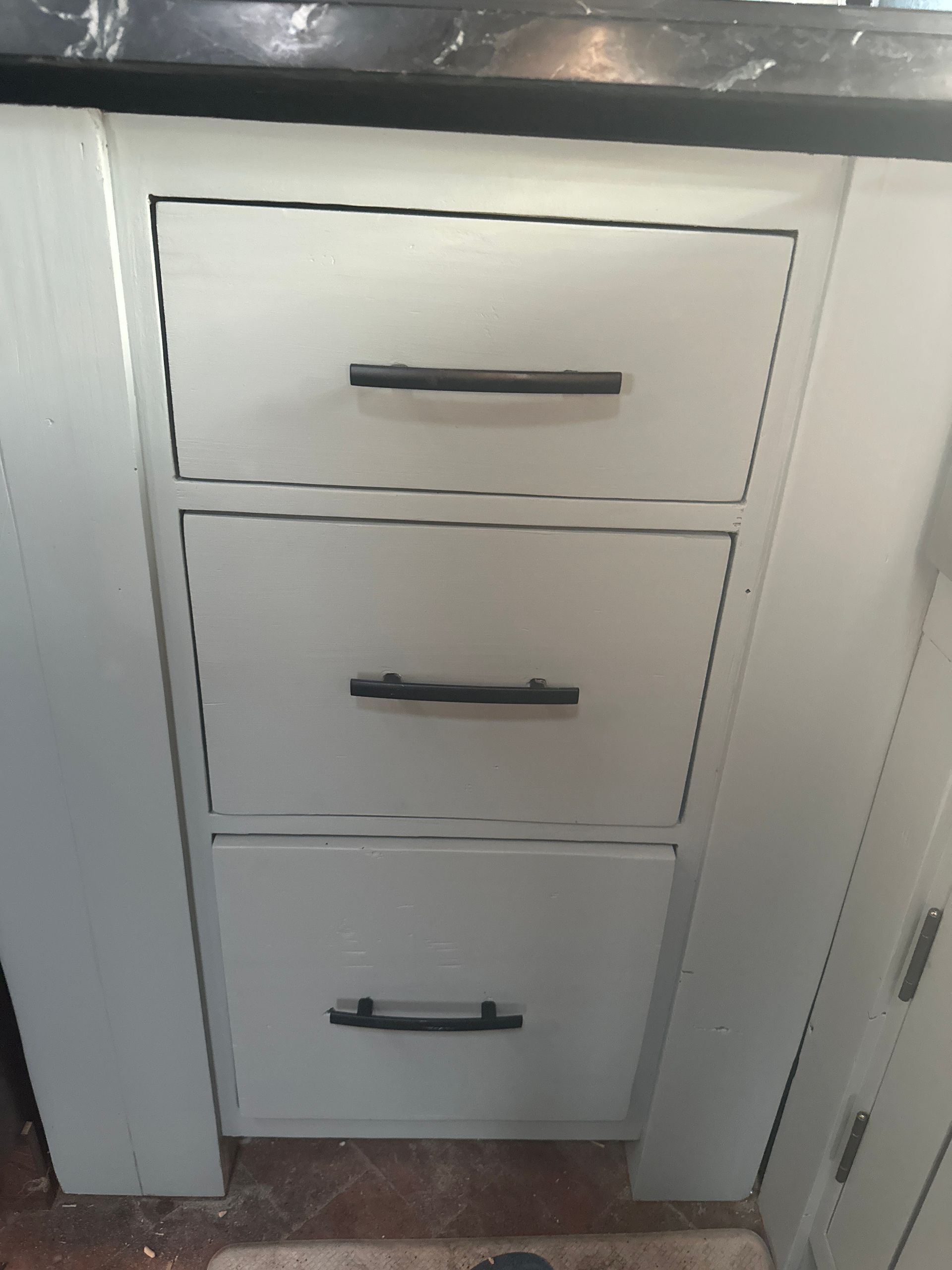 Three stacked white cabinet drawers with black handles in a narrow closet opening.