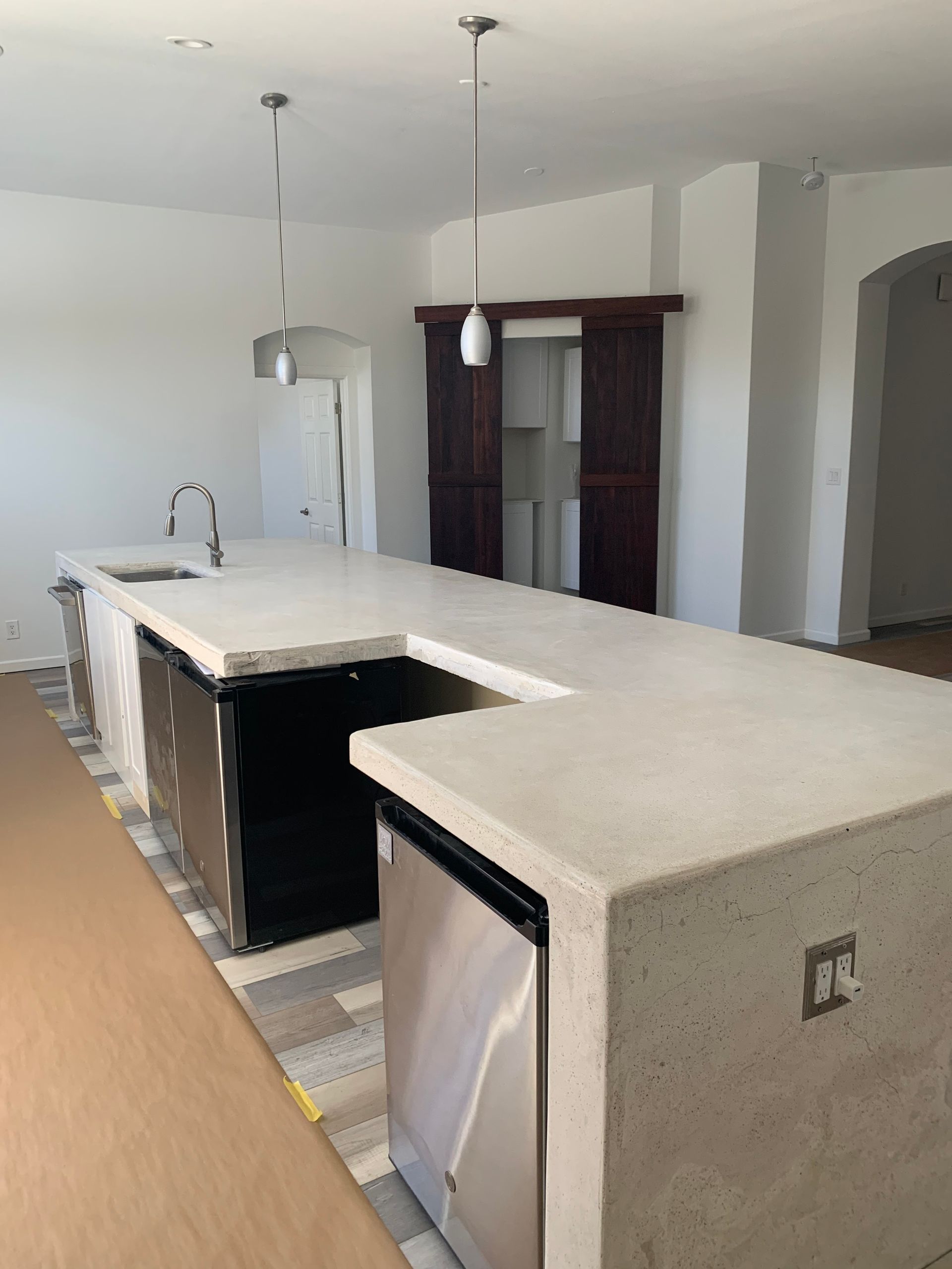 Modern kitchen with large white island, pendant lights, and stainless dishwasher.