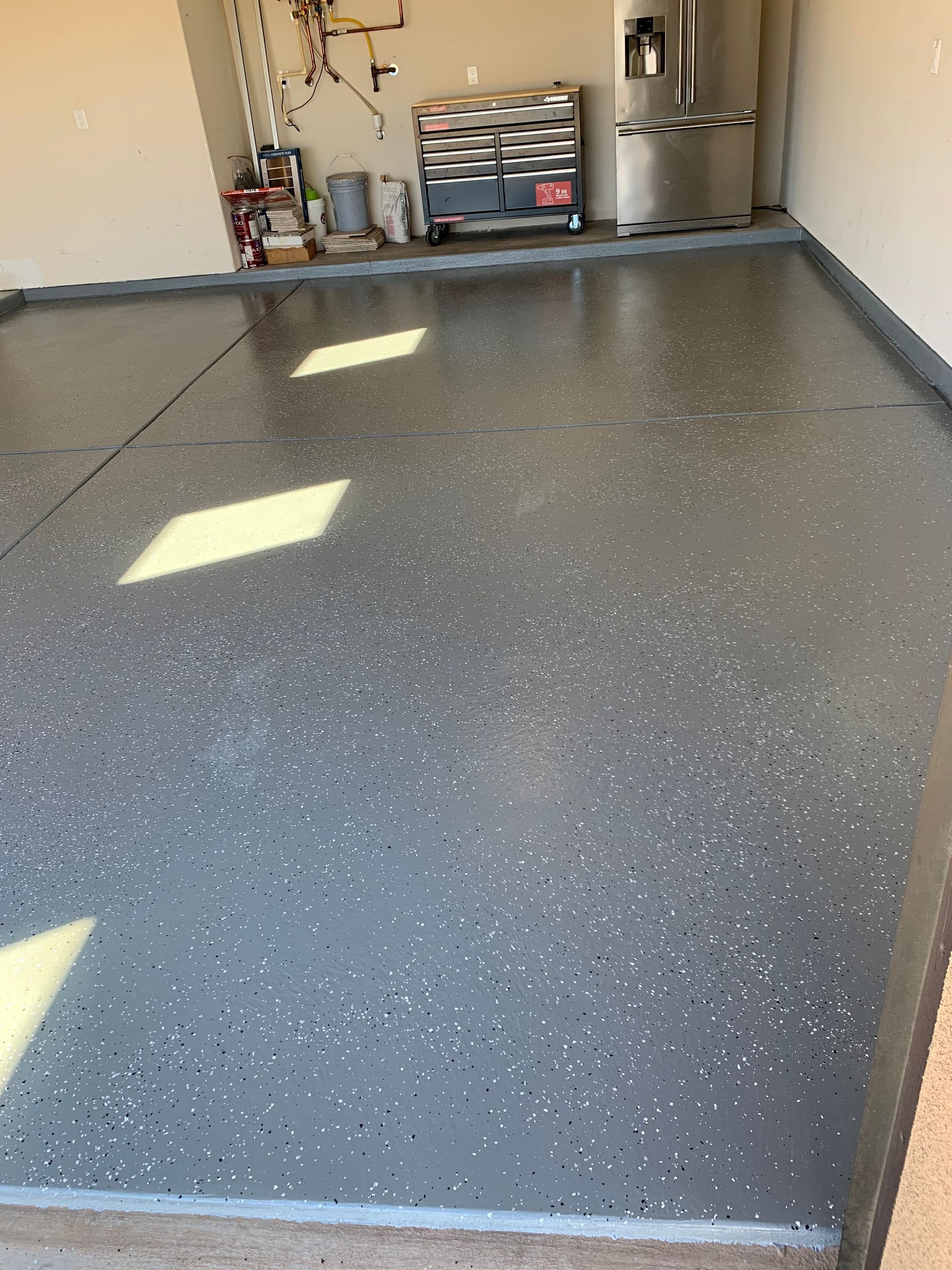 Empty garage with a speckled gray epoxy floor and shelves at the back.