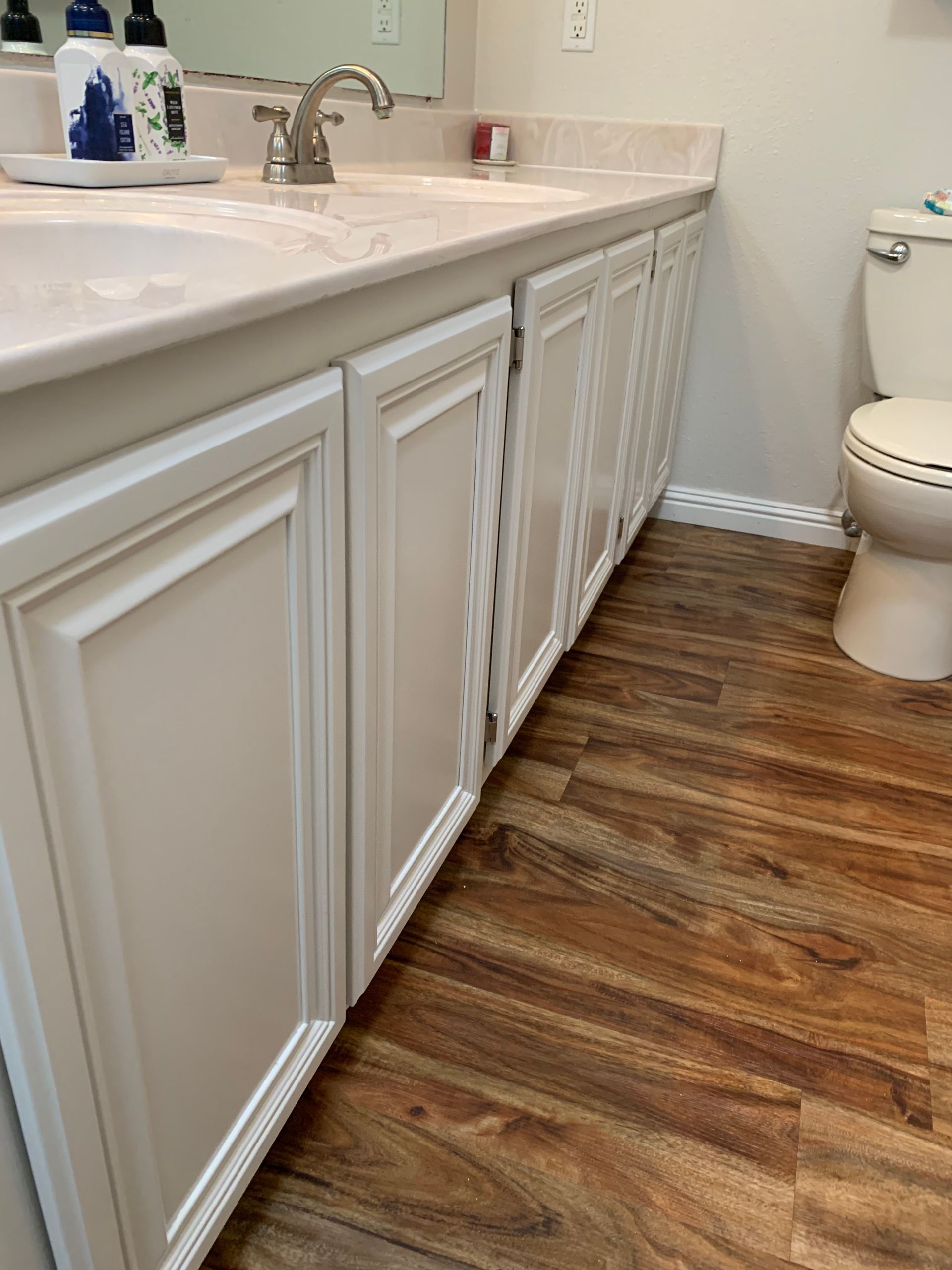 Bathroom vanity with white cabinets, marble countertop, and wood-look floor beside a toilet